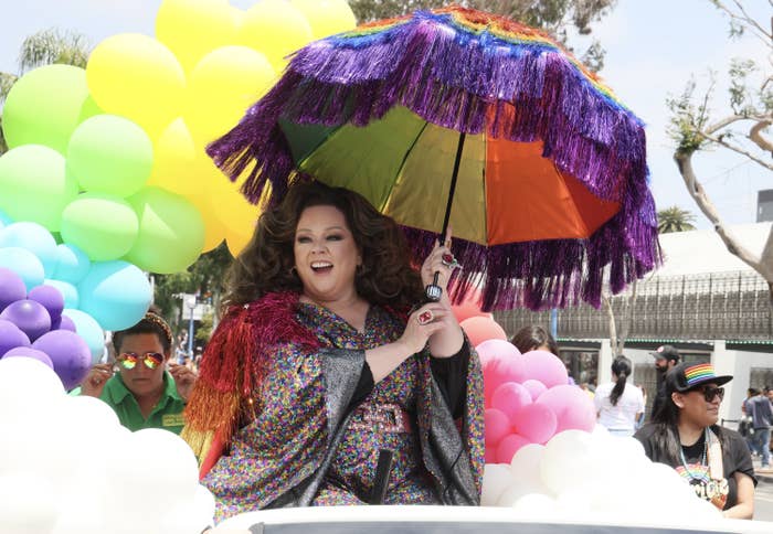 Melissa McCarthy riding in the parade holding a huge fringed Pride-colored umbrella