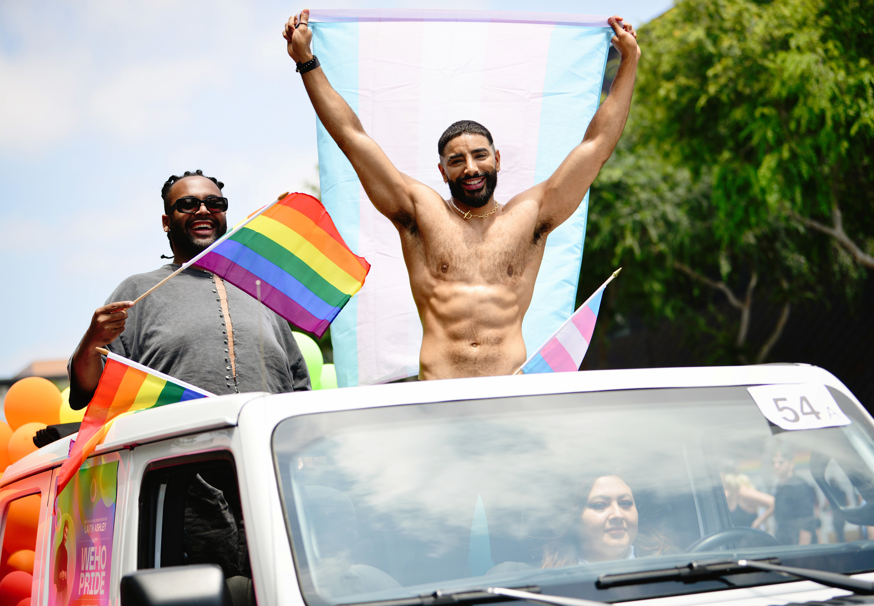 Laith Ashley at the parade standing in a car holding up the Transgender flag