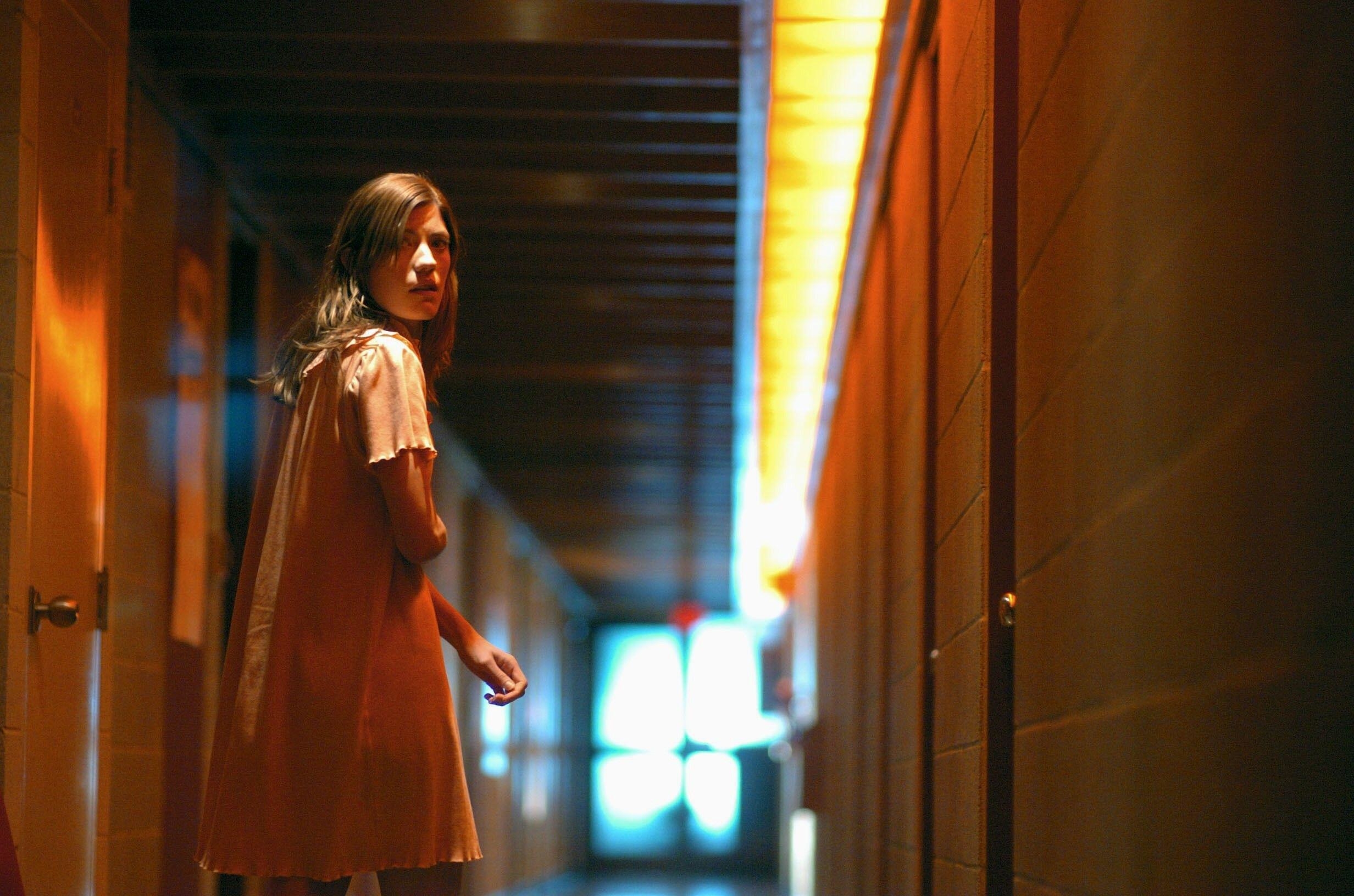 A scared young woman stares down a dimly lit hallway
