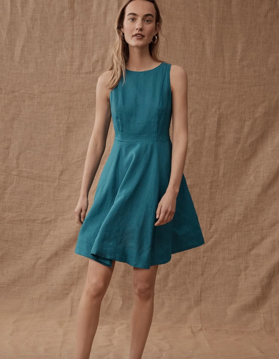 a model wearing a teal linen skater mini dress in front of a curtain