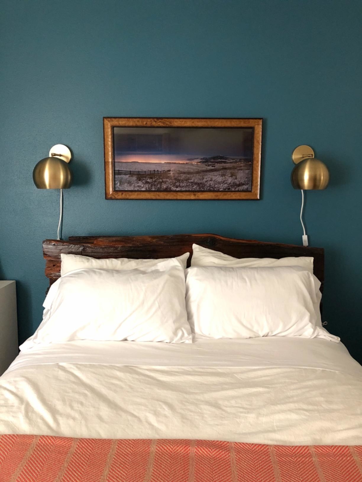 Reviewer&#x27;s photo of two wall sconces in the color Willow (Brass), hung on either side of a double bed