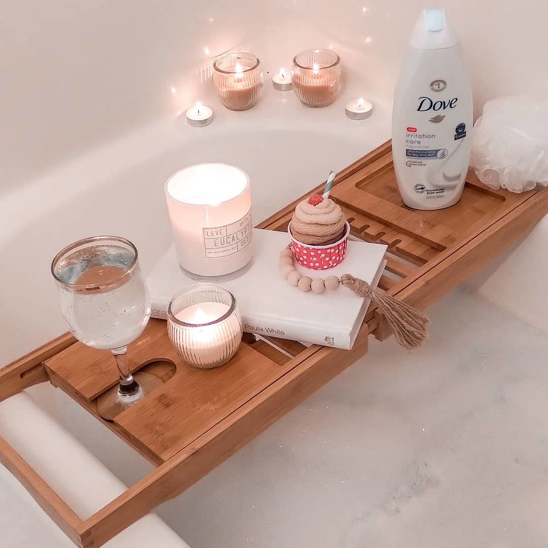the bamboo tray over a bathtub with candles and other various items placed on top