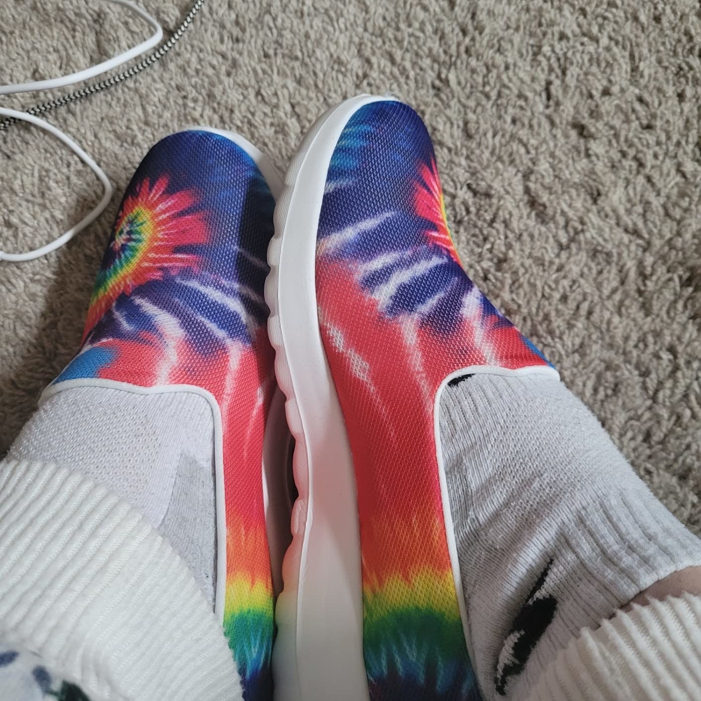 A reviewer wearing a  pair of tie dye shoes