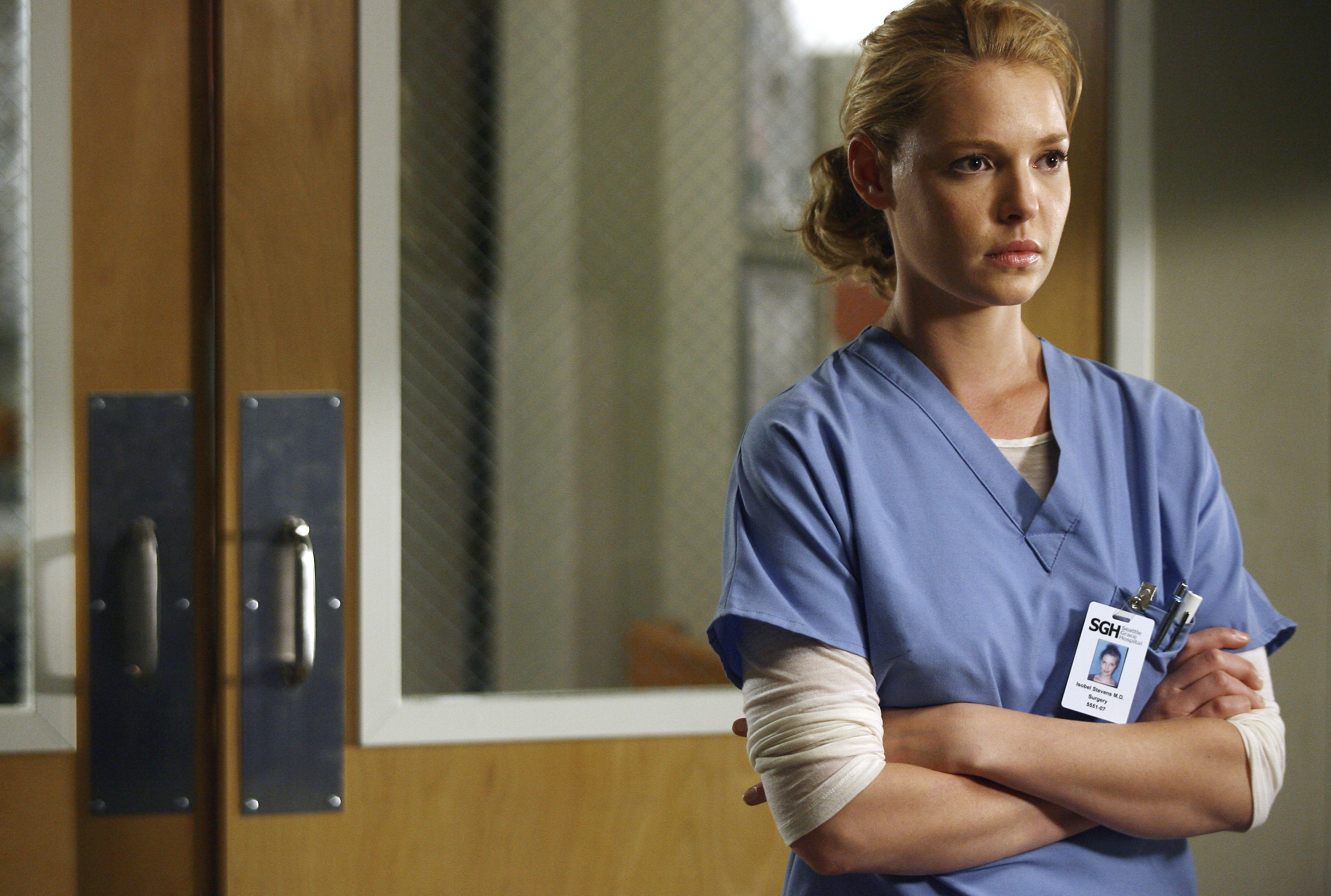 Izzie in her scrubs stands with her arms folded