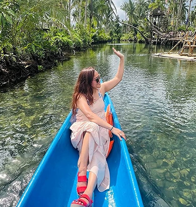 same reviewer in red wedge sandals waving in boat on tropical lake