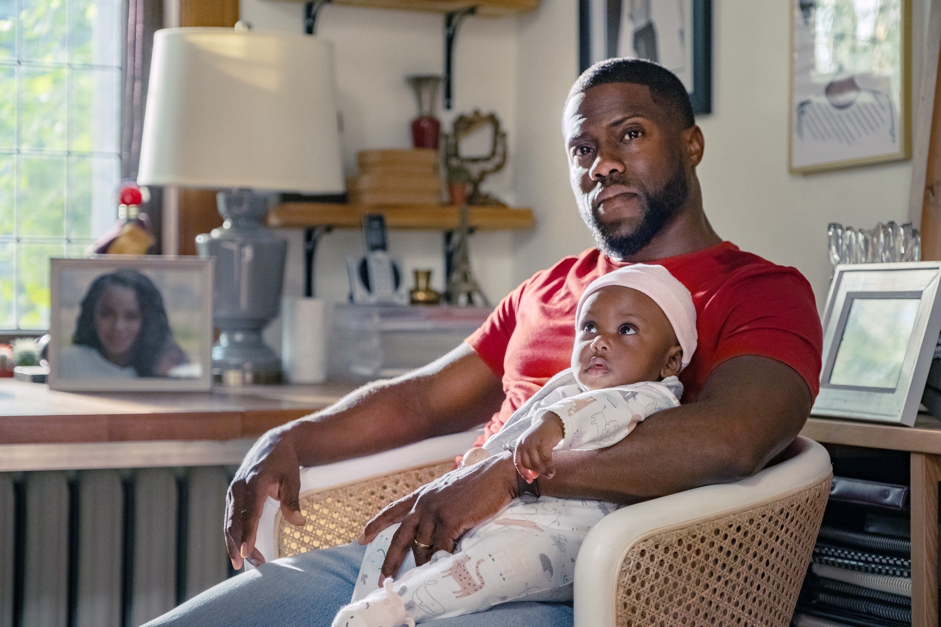 Kevin Hart holding a baby while sitting in a chair in the movie Fatherhood