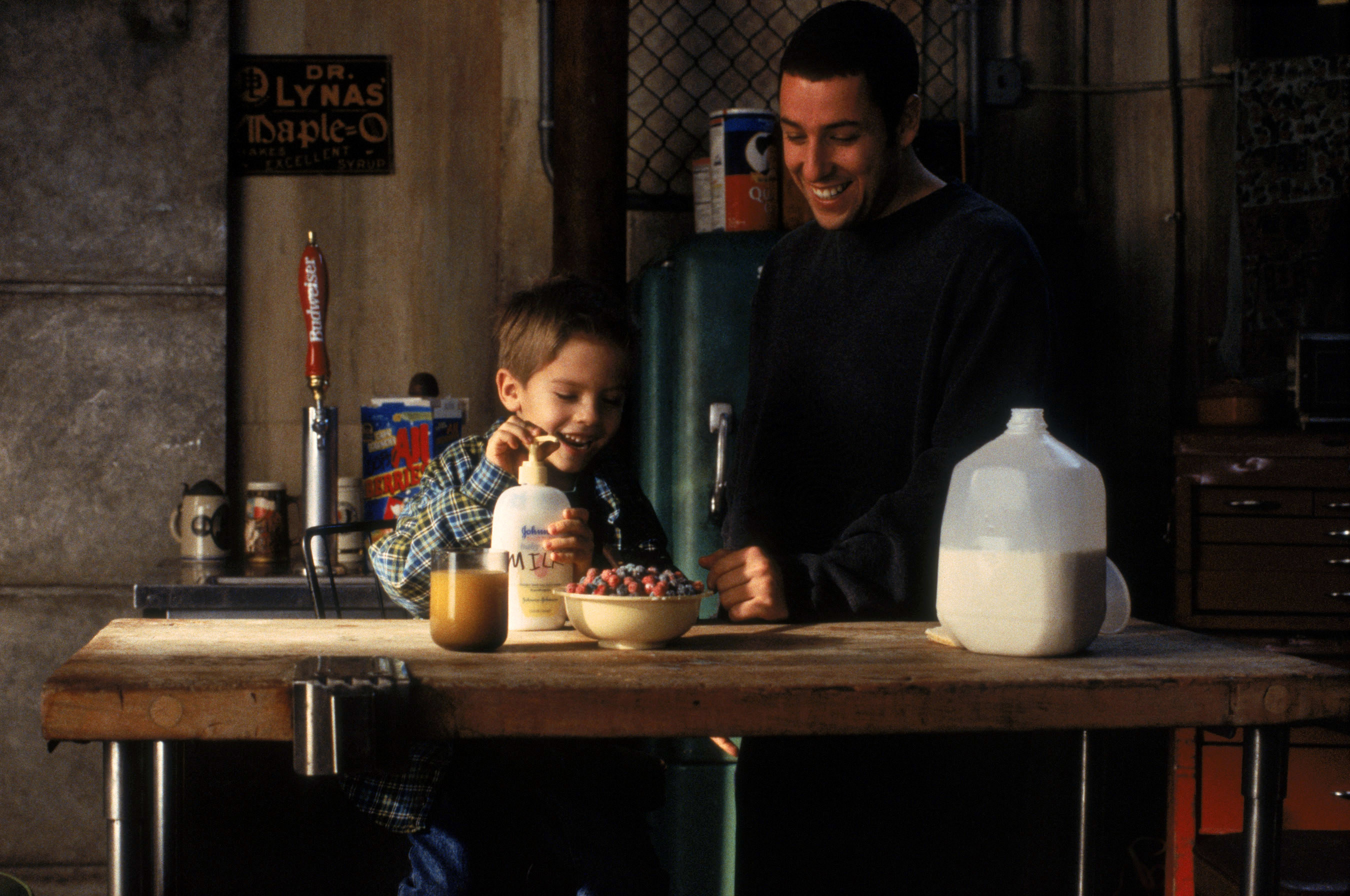 Adam Sandler looks on as a small child, played by twins Cole and Dylan Sprouse,  makes a bowl of cereal in the kitchen in a scene from the film Big Daddy