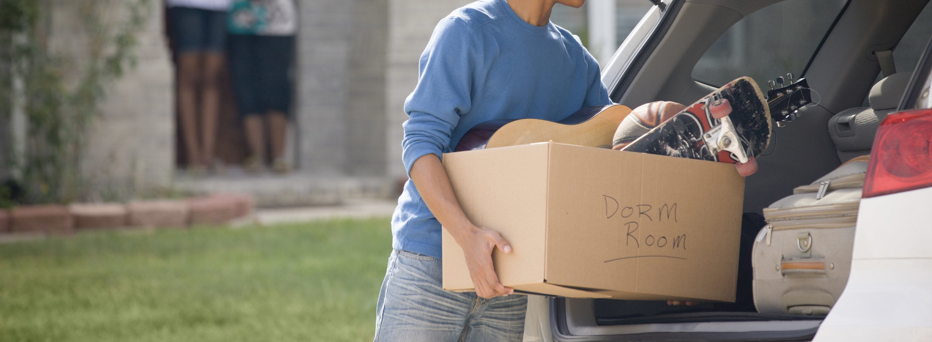 A young person putting a box of belongings into the back of a car