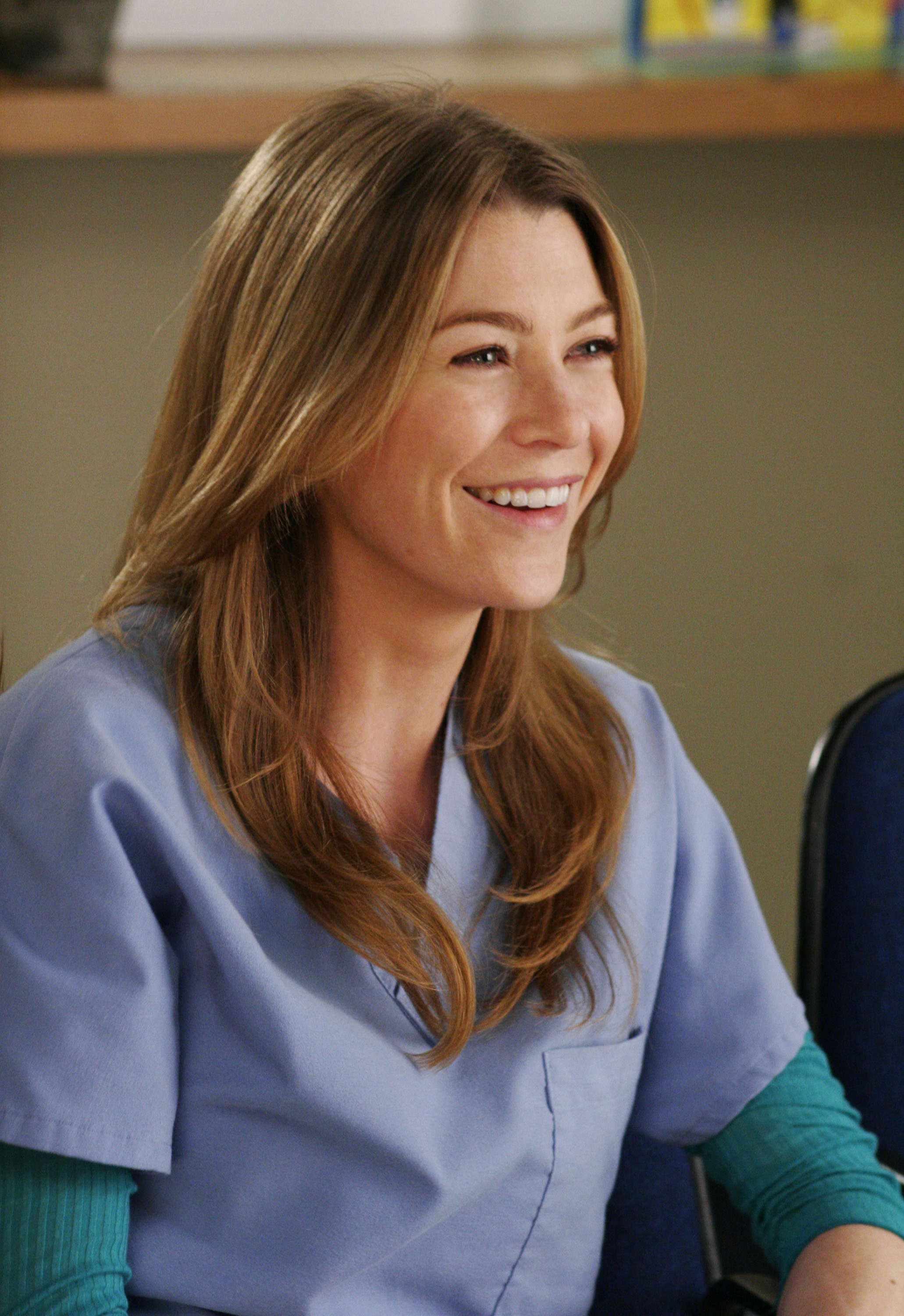 A close-up of Meredith Grey, in scrubs, smiling