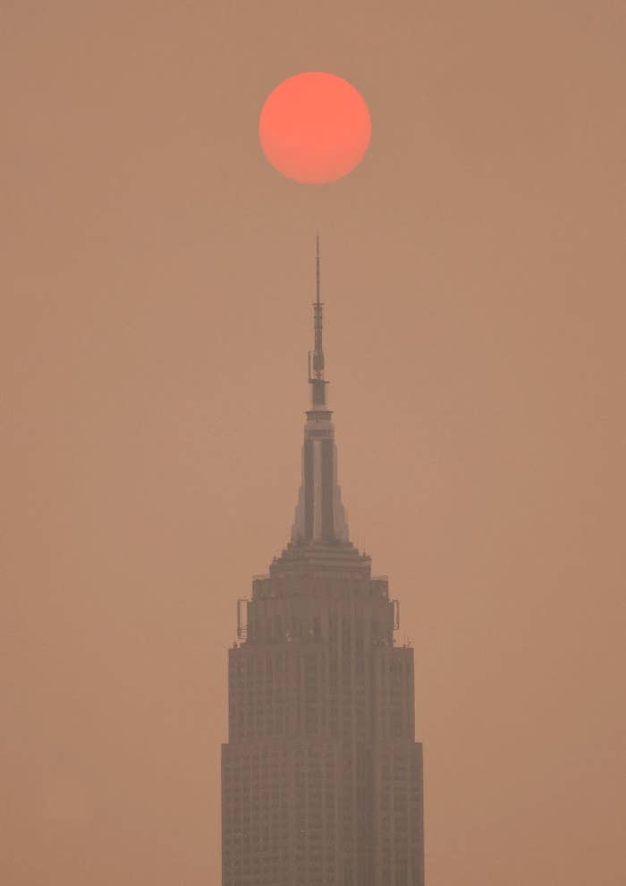 The sun is shrouded as it rises in a hazy, smoky sky behind the Empire State Building