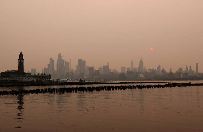 The sun is shrouded as it rises in a hazy, smoky sky behind the Empire State Building and the skyline of midtown Manhattan