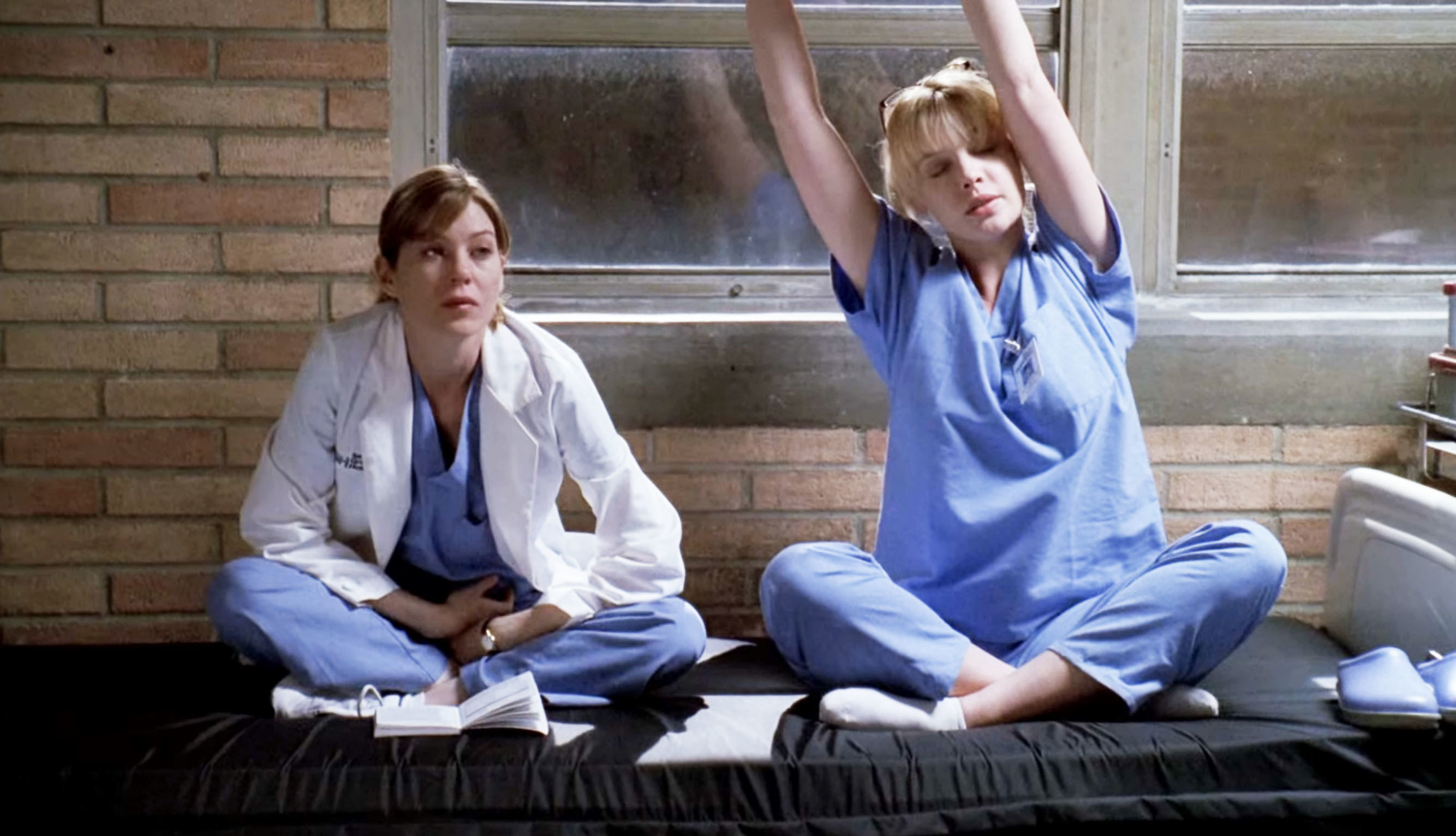 Meredith和Izzie跨行坐在医院床上,Izzie伸展双臂头顶