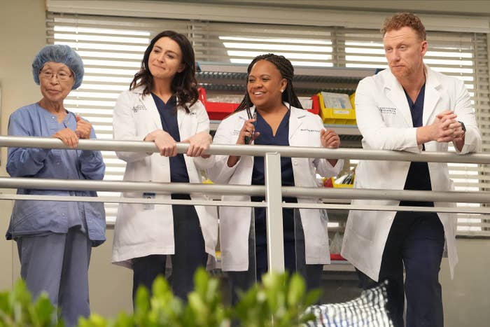 Four medical professionals standing by a railing on an upper floor of the hospital in a scene Grey&#x27;s Anatomy