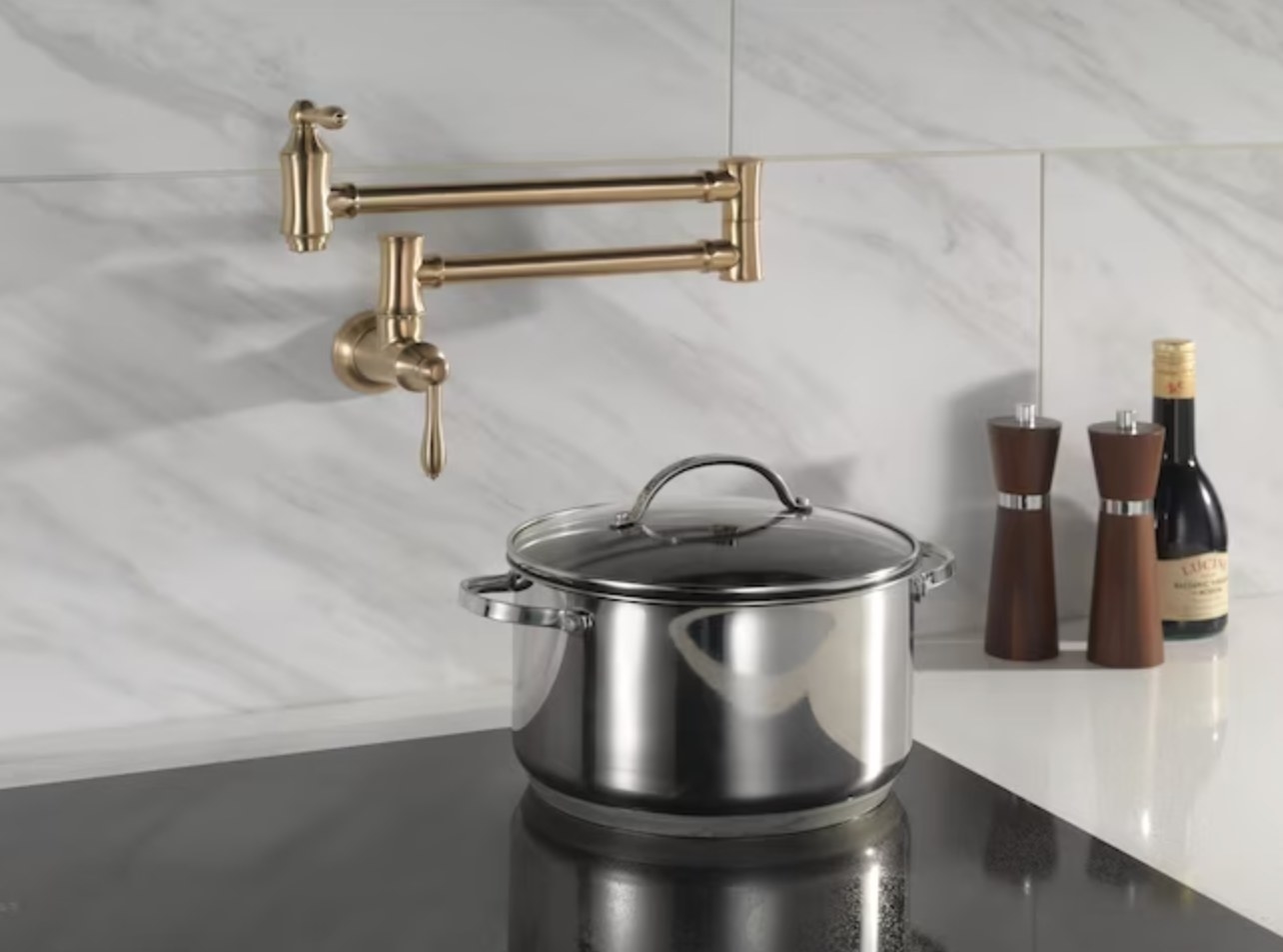 the gold faucet installed in a wall above a glass cooktop with a large pot on top