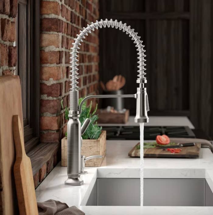 the silver arched faucet with a stream of water, in a decorated kitchen space