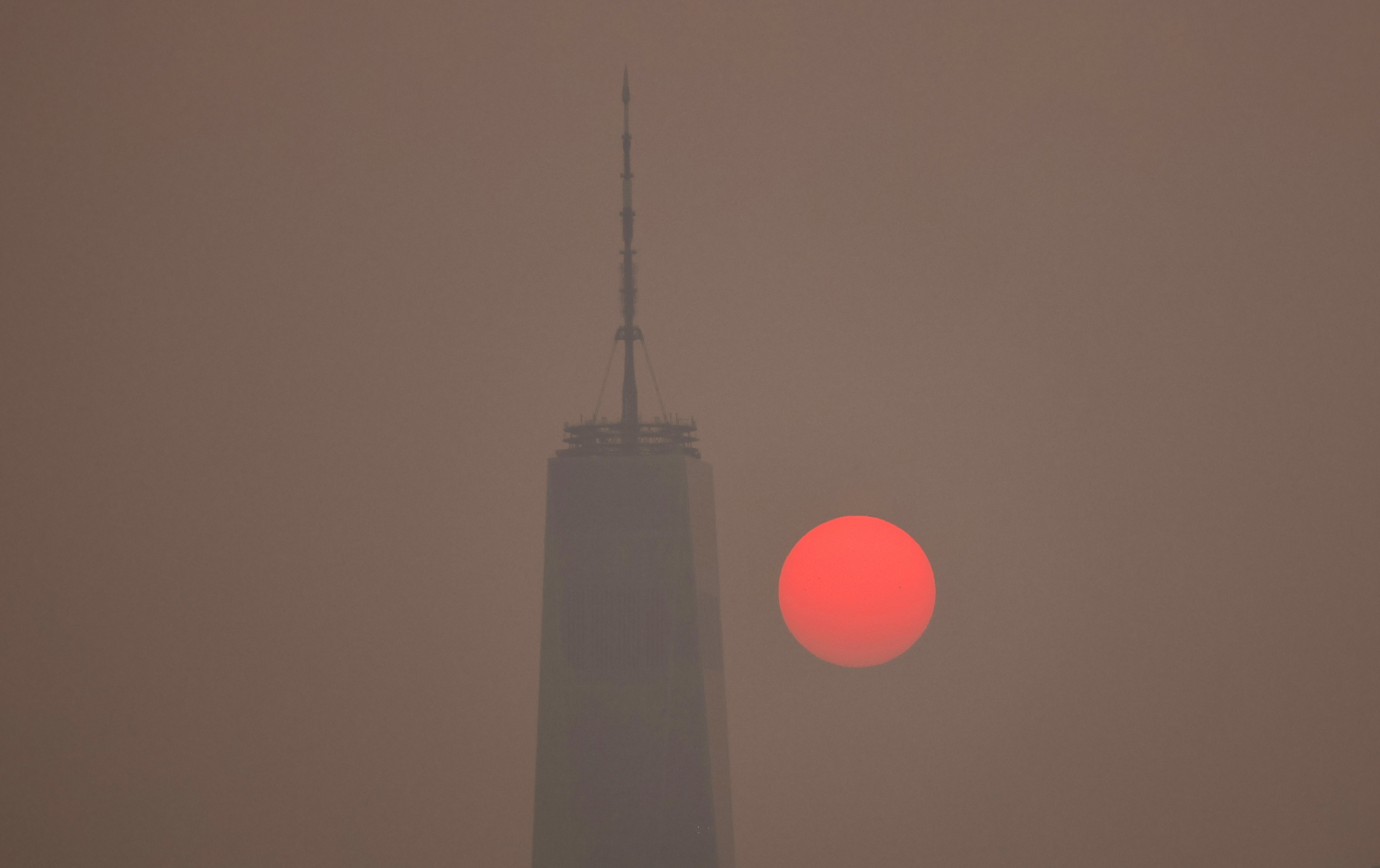 A close-up of the sun which looks neon orange-red due to the smoke