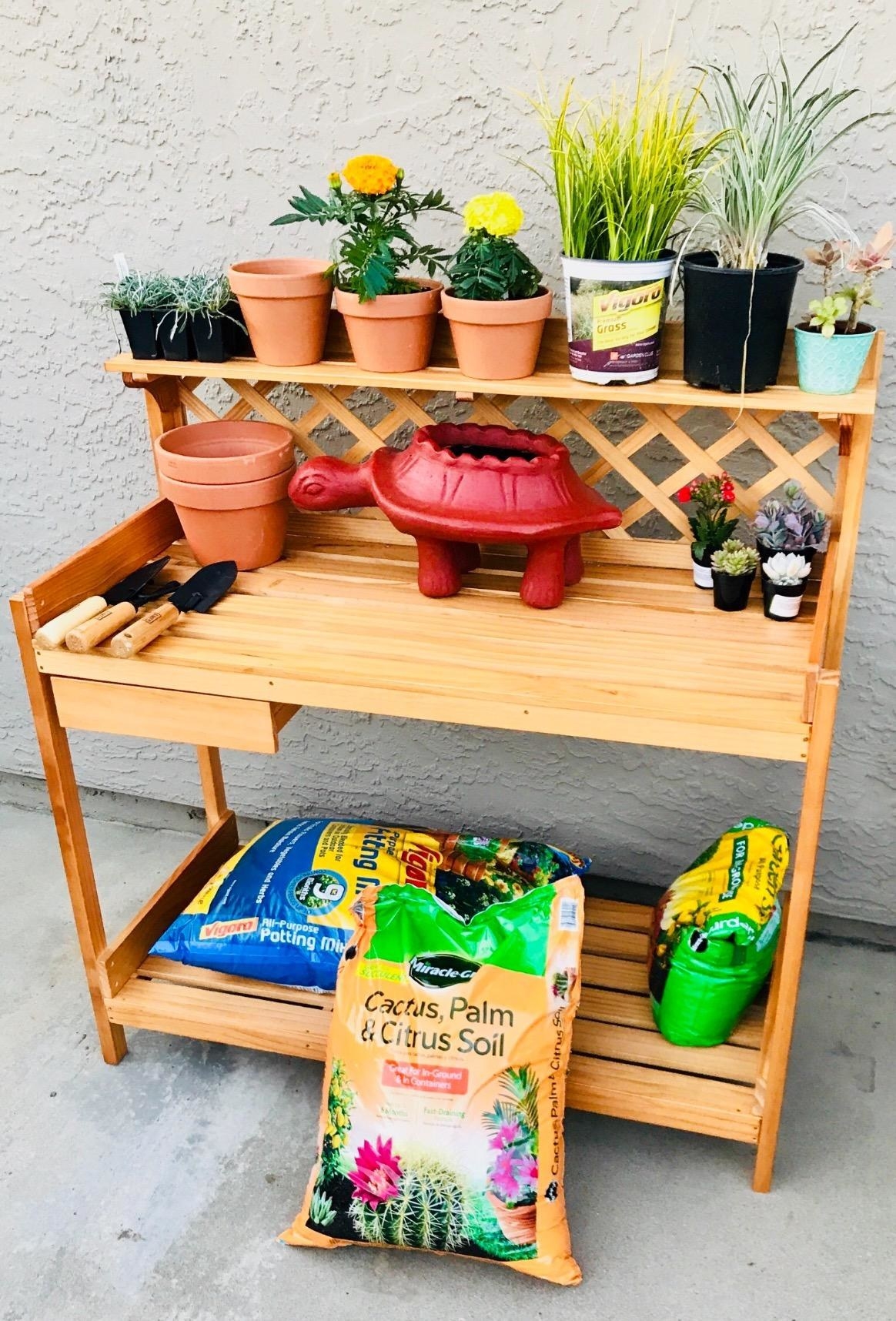 Reviewer&#x27;s photo of the potting bench with pots, tools, bags of soil, and other gardening supplies stored on it
