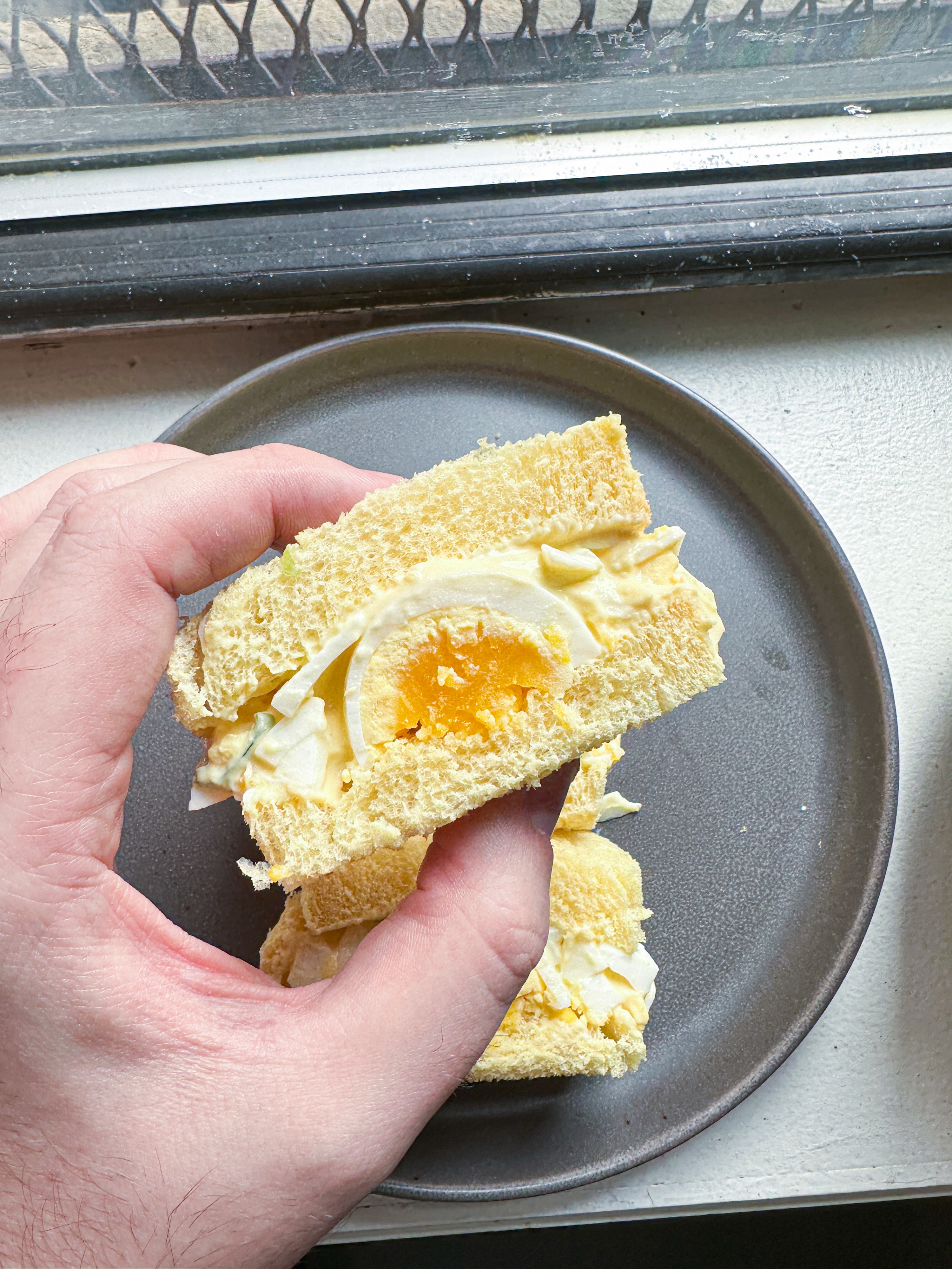 author holding a japanese style egg sandwich cross section with golden yolk revealed