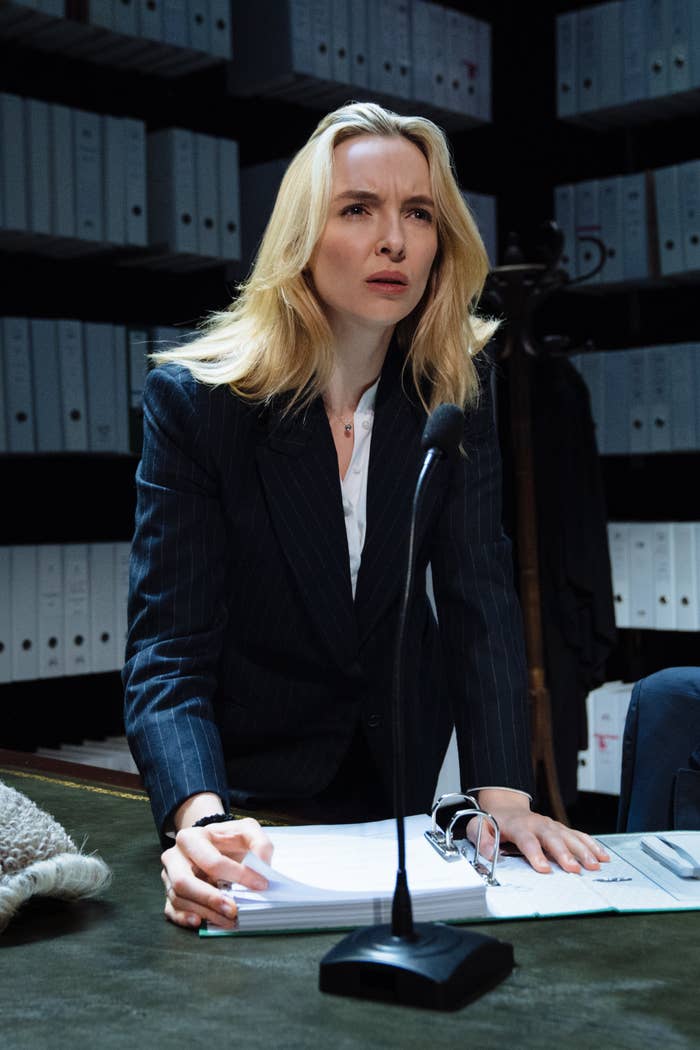 Jodie in front of a microphone and looseleaf notebook on a desk in a scene from the play
