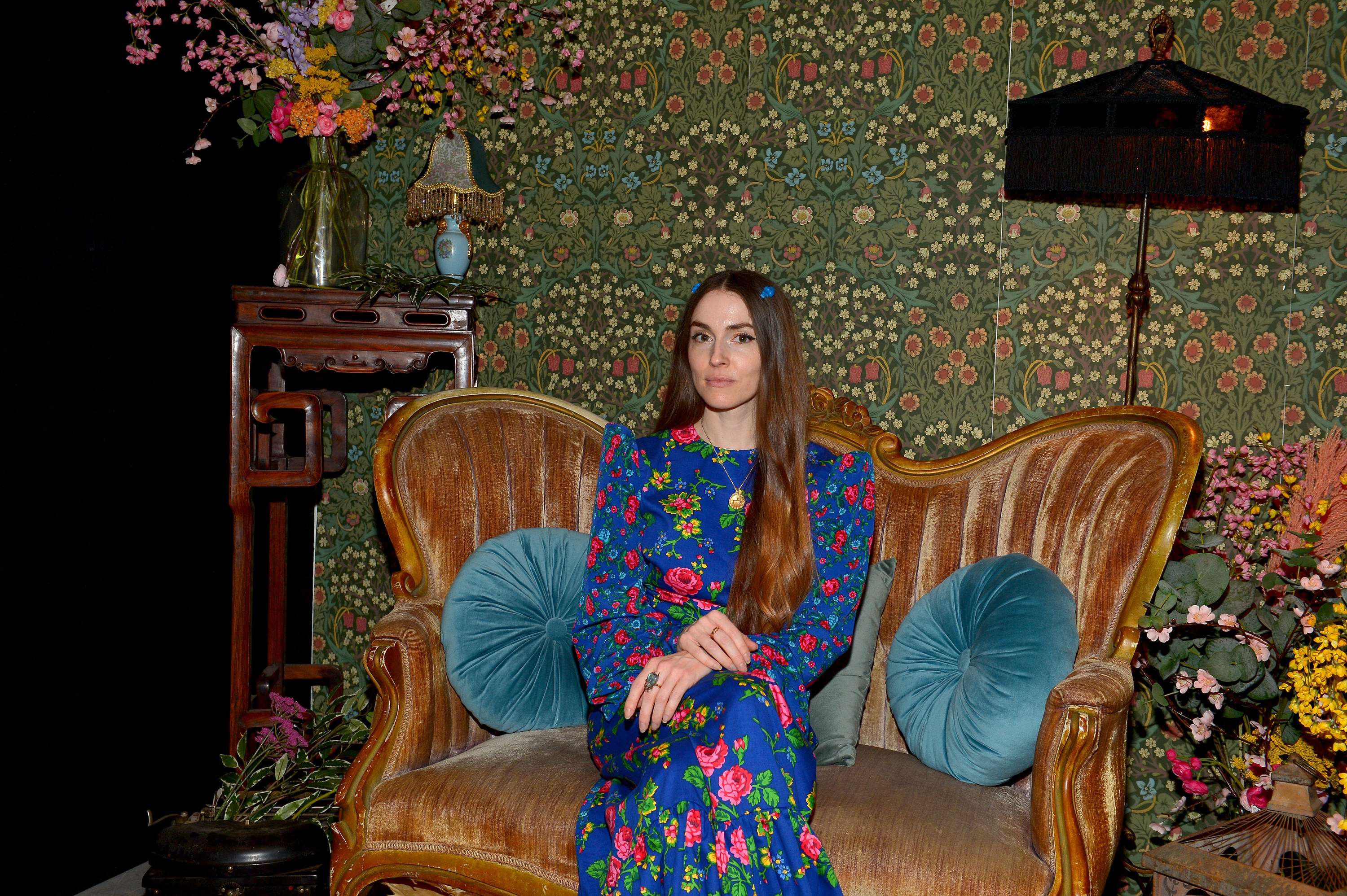Close-up of Anna sitting in a love seat and wearing a long-sleeved floral dress