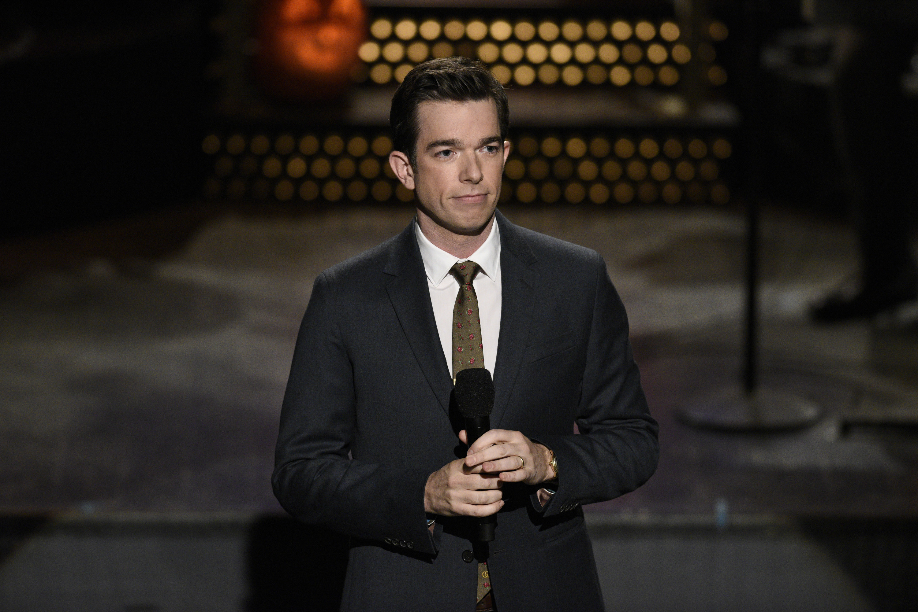 John in a suit and tie and holding a microphone