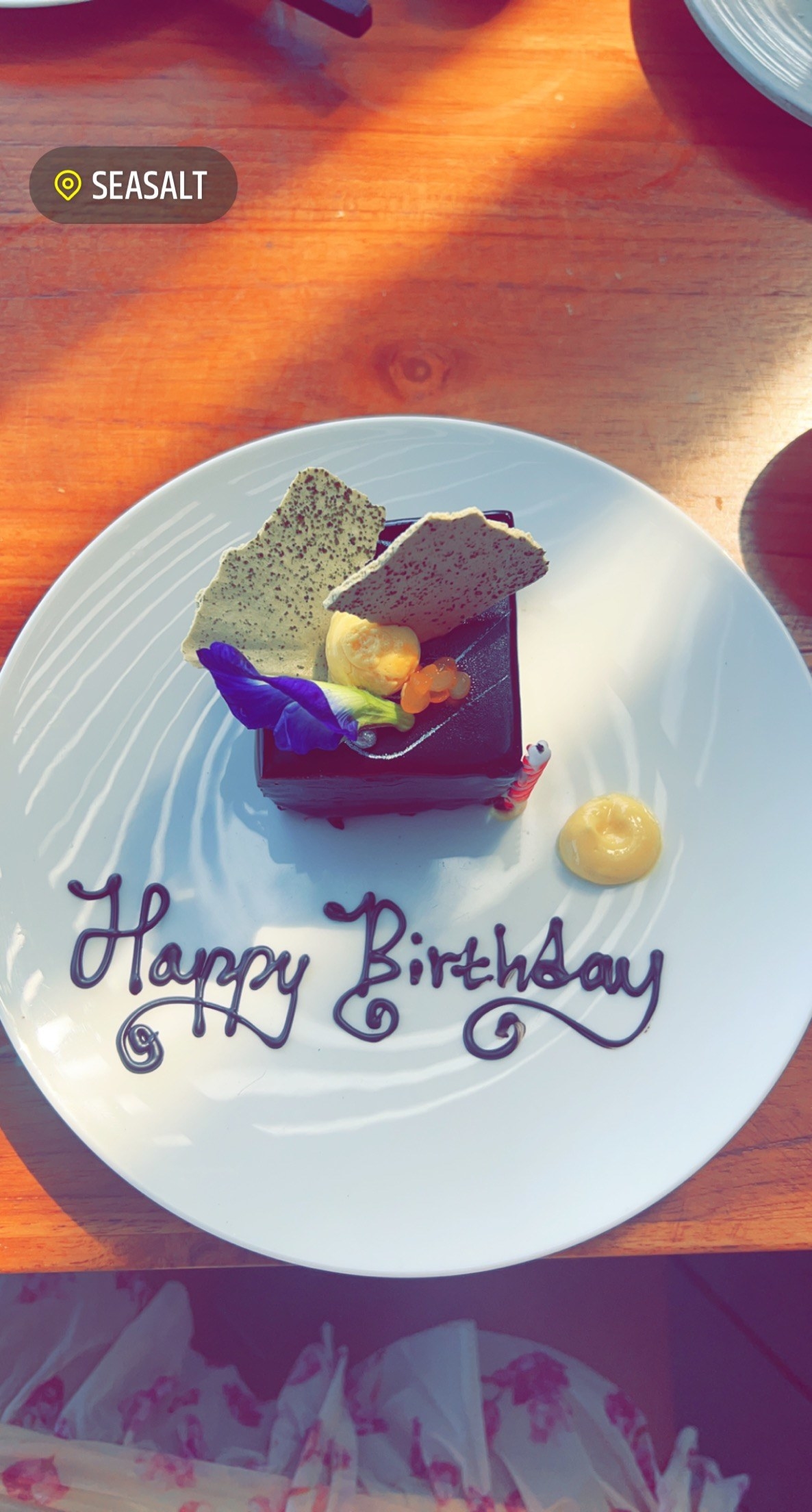 a small square of chocolate cake on a white plate that says "Happy Birthday"