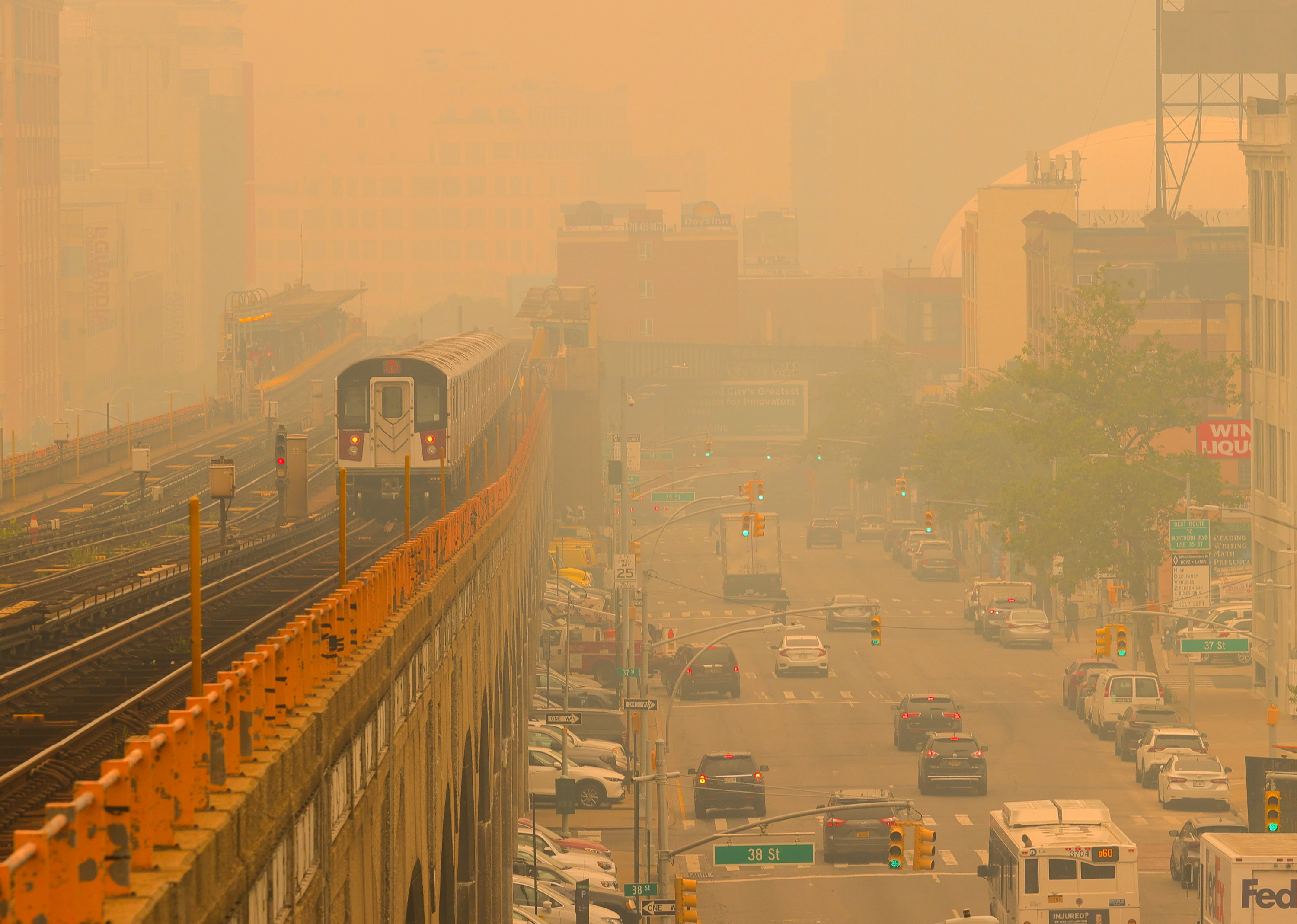 An above ground subway train moves through haze as cars do the same on the right