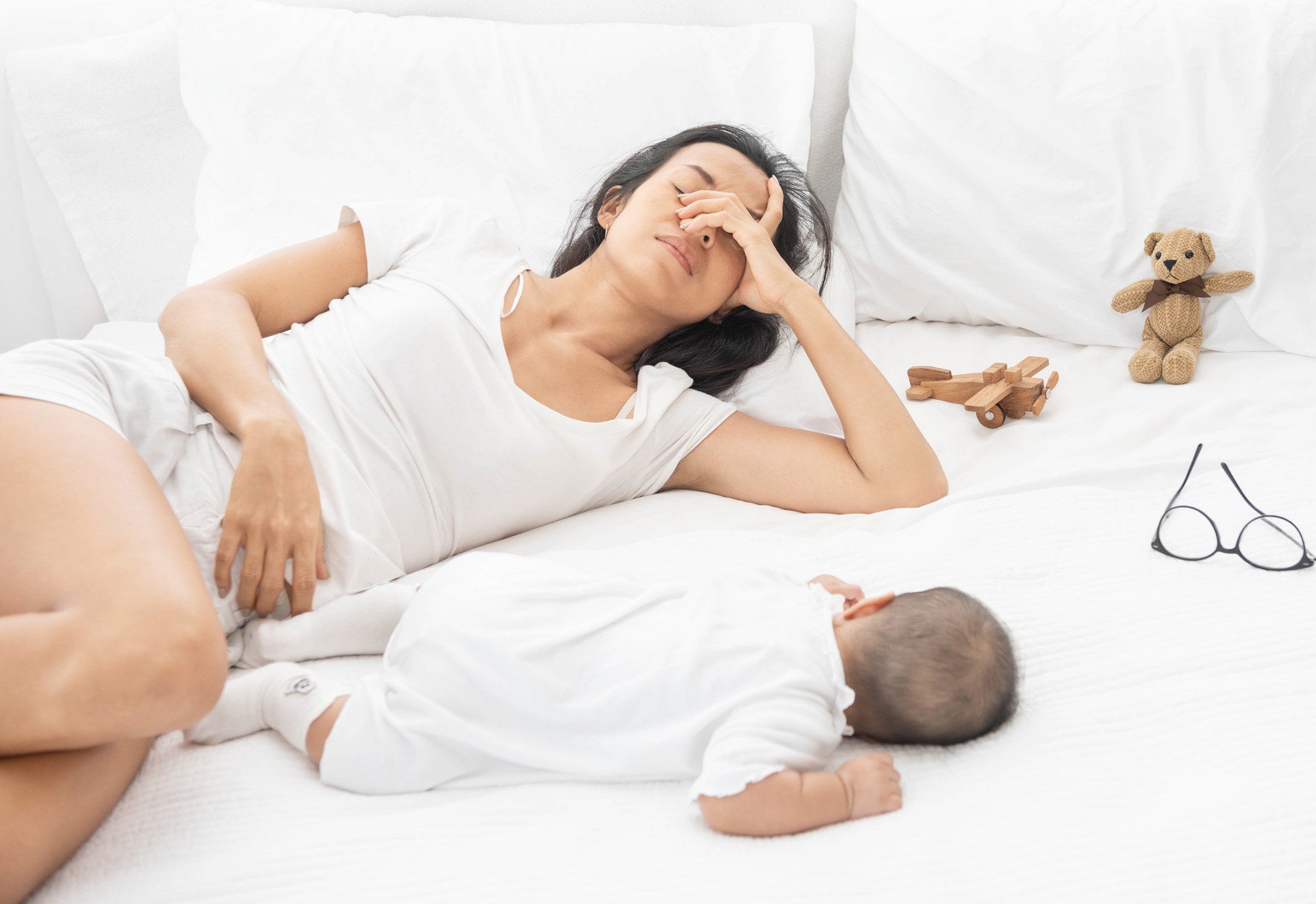 tired mom with hand over her face as she lies down with baby