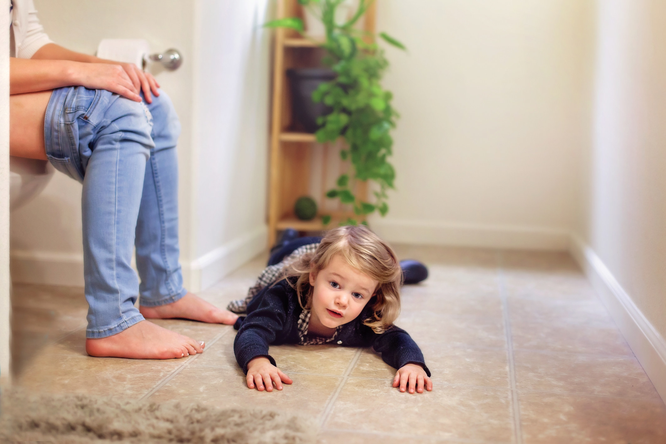 toddler on the bathroom floor with the parent uses the toilet