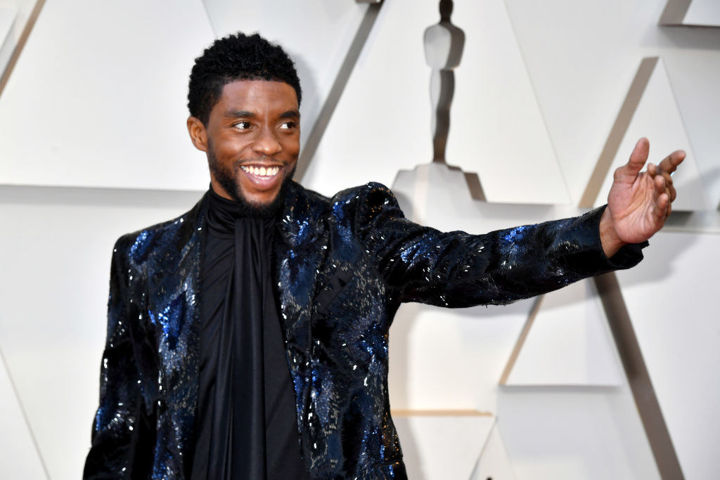 Chadwick wearing a sparkly jacket, smiling, and raising his arm