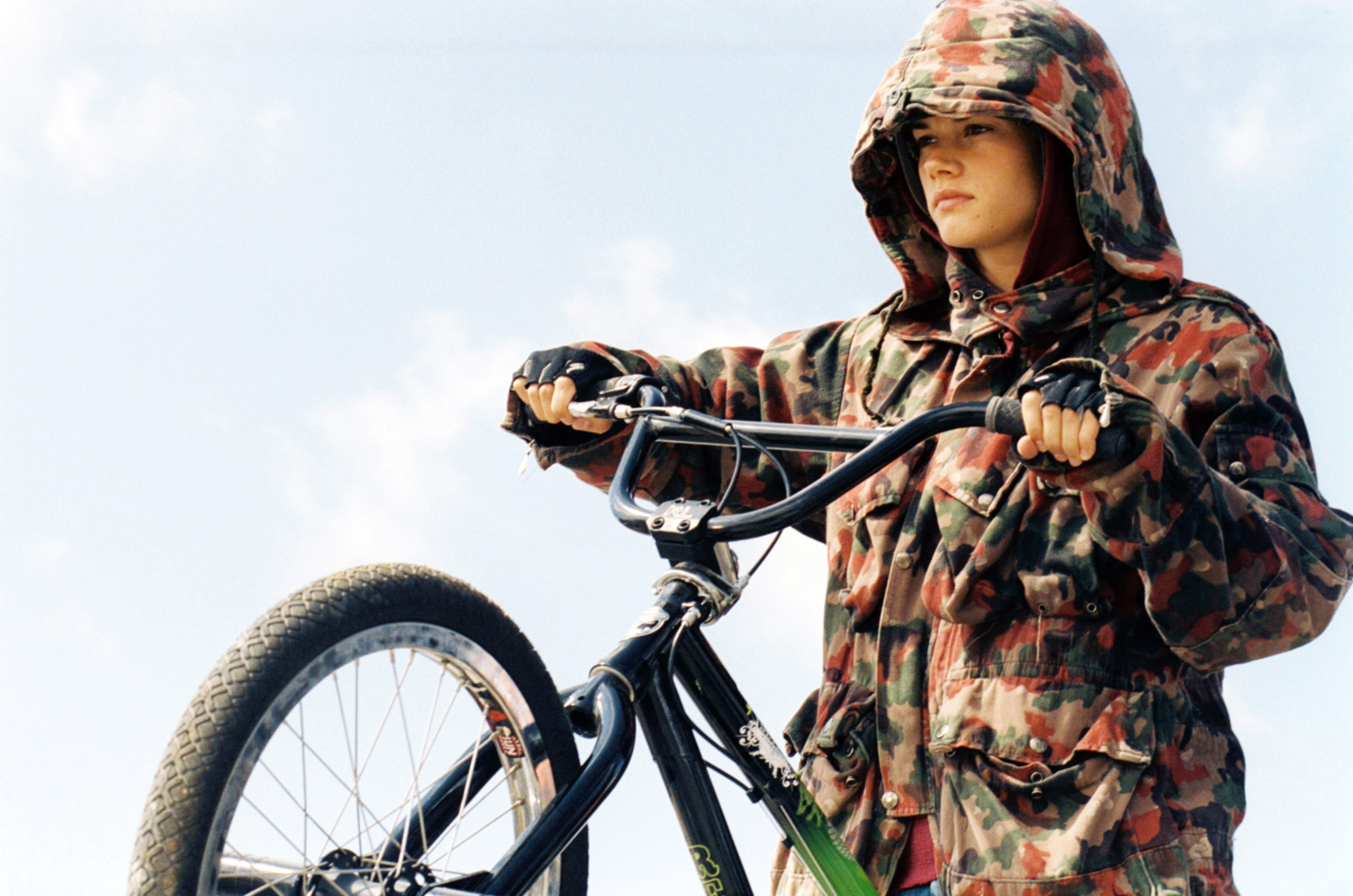 A girl in a camo jacket holds onto a bike.