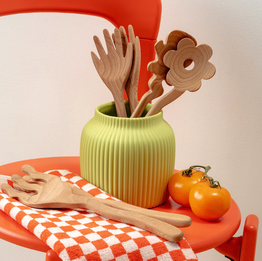 serving utensils in a green vase on an orange table