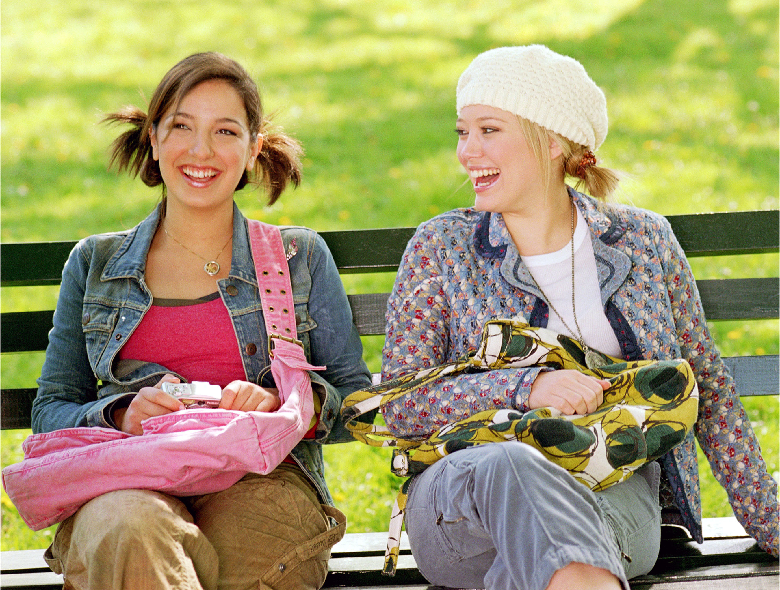 Two teens sit next to each other and laugh on a park bench.