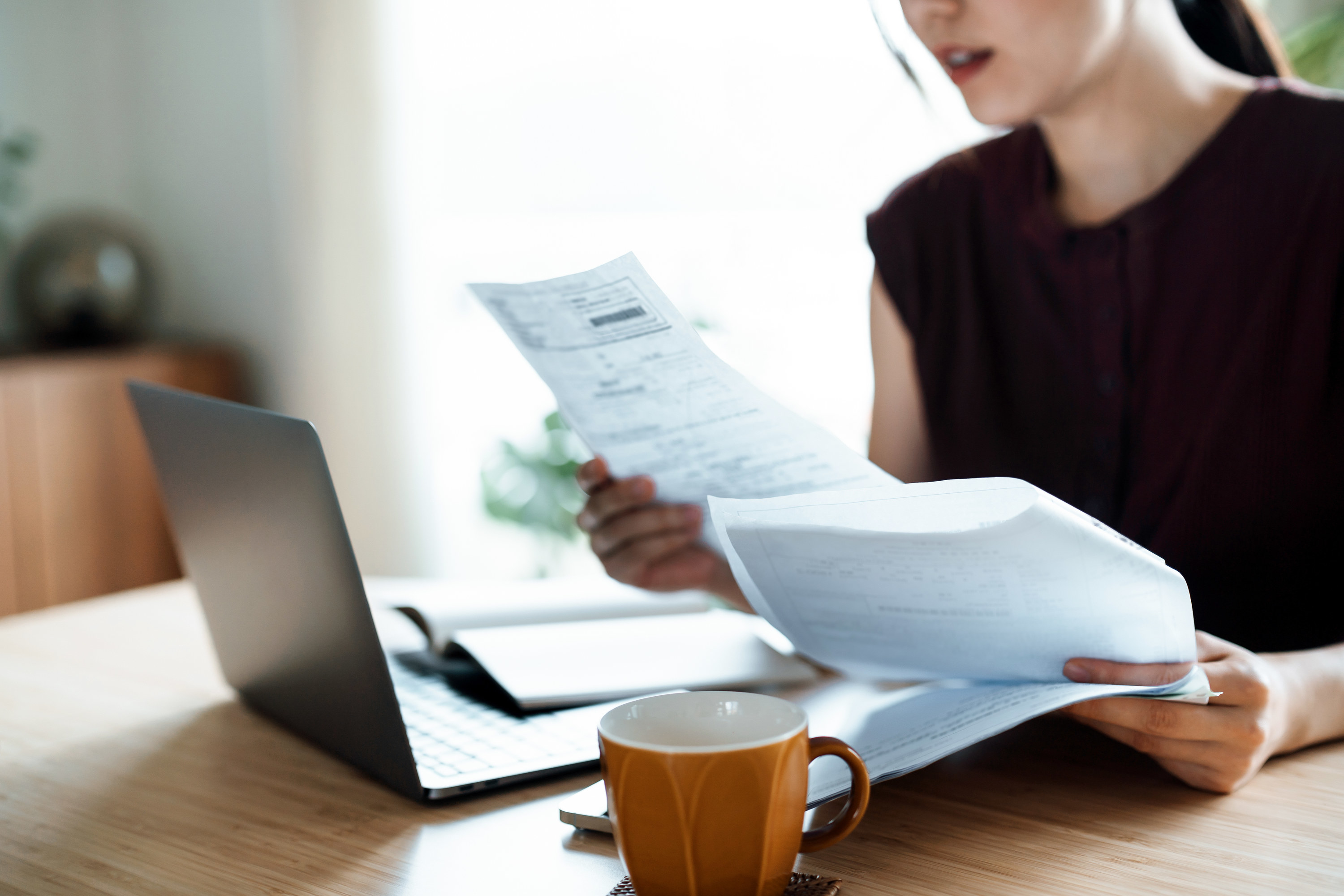 a person going over papers at their table in front of a laptop