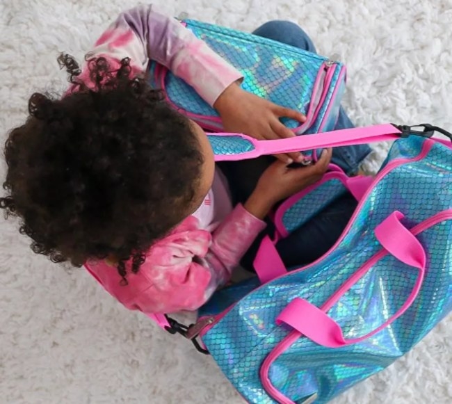 A child holding a blue mermaidlike fabric toiletry bag