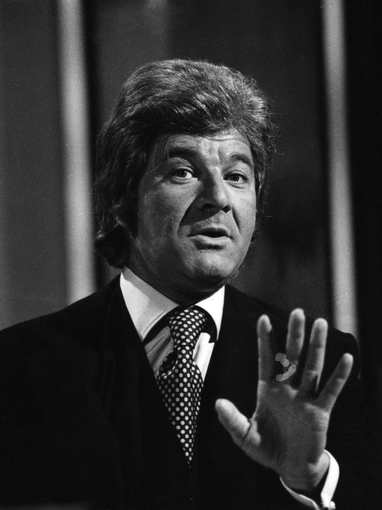 Close-up of Shawn in a suit and tie, with his hand held in front of him