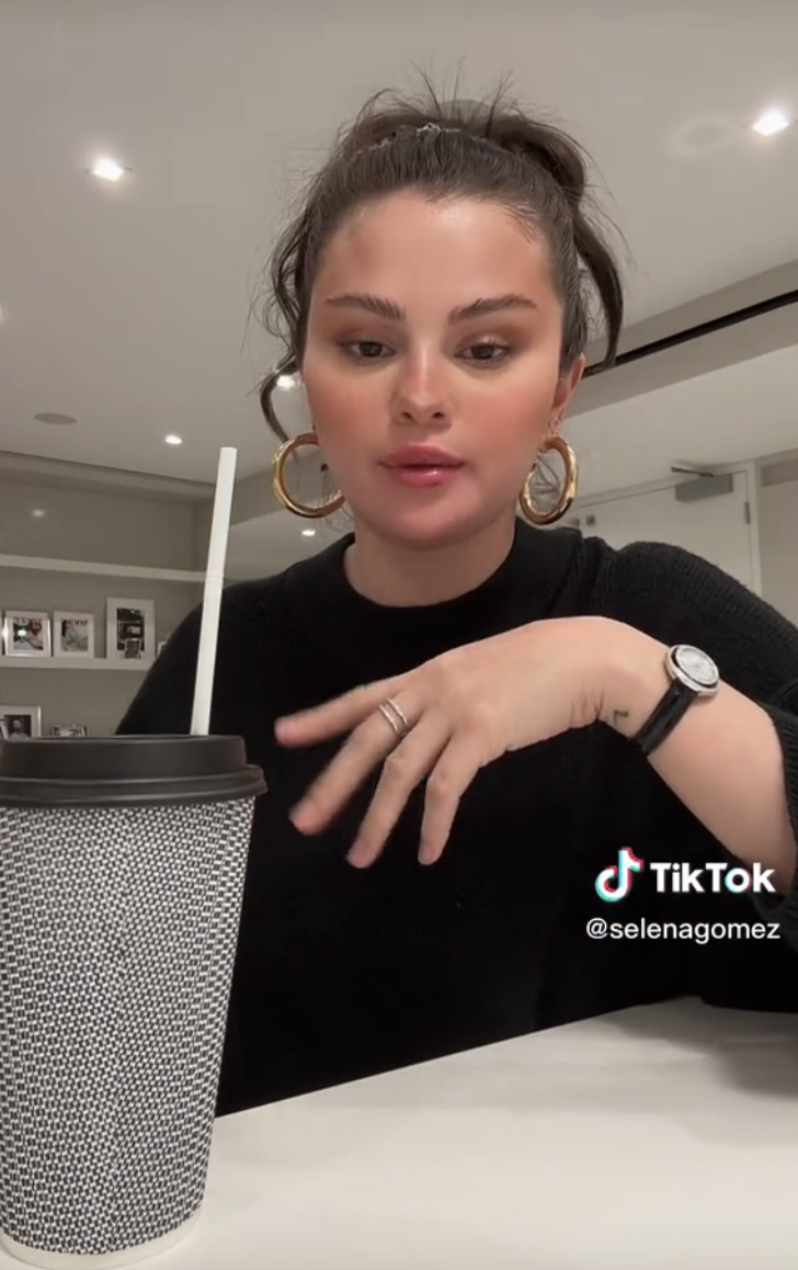 Screenshot of Selena&#x27;s TIkTok where she&#x27;s sitting with a large drink cup and straw and wearing hoop earrings
