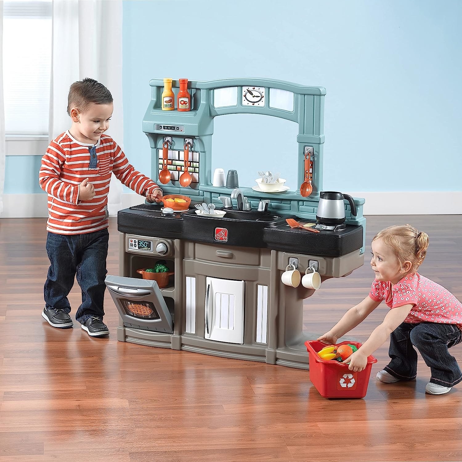 Two child models playing in and around plastic kitchen play set
