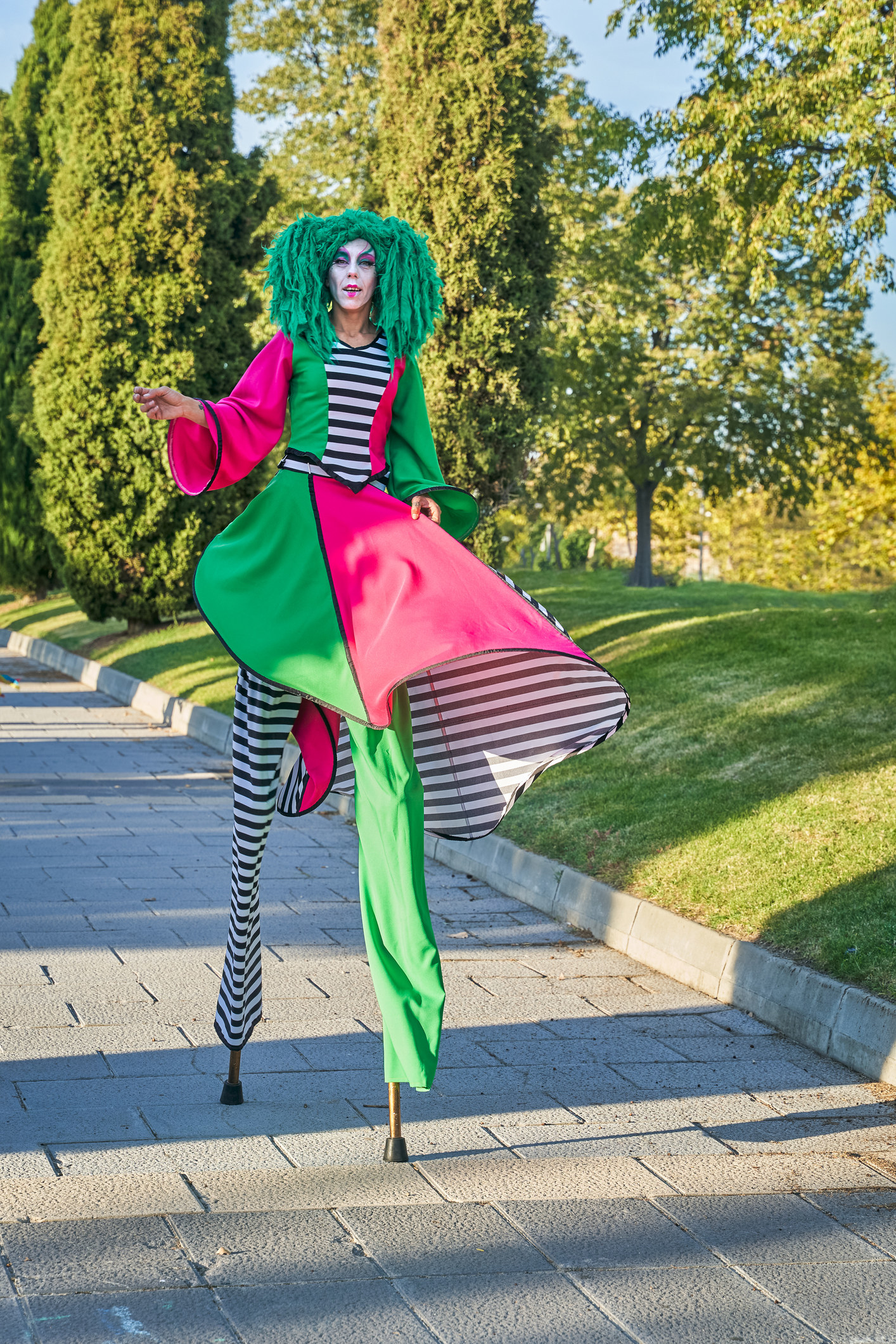 A person in a clownish costume walking on stilts outside