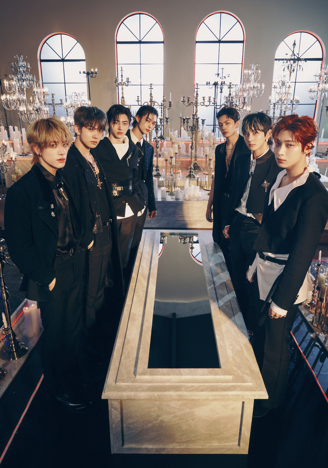 K-pop group Enhypen posing for their album Dark Blood by standing around a coffin with a mirror on it