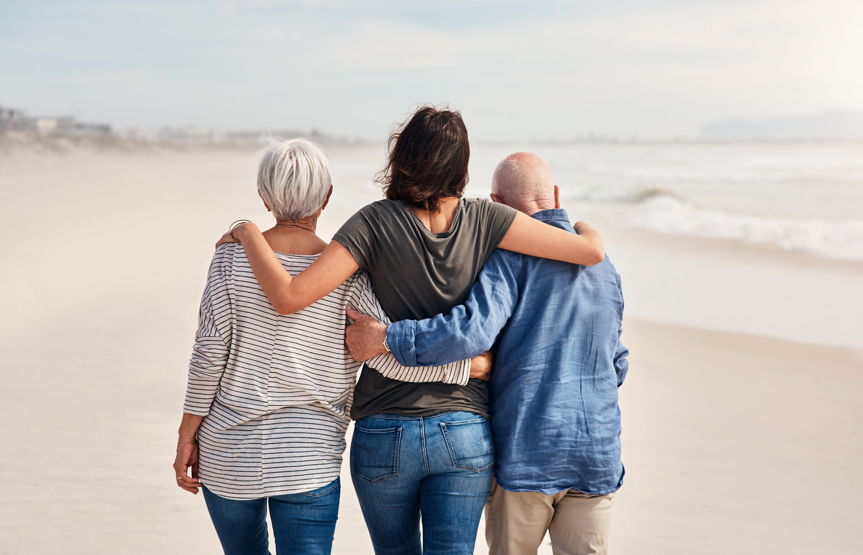 A woman walks on the beach with her parents by her side