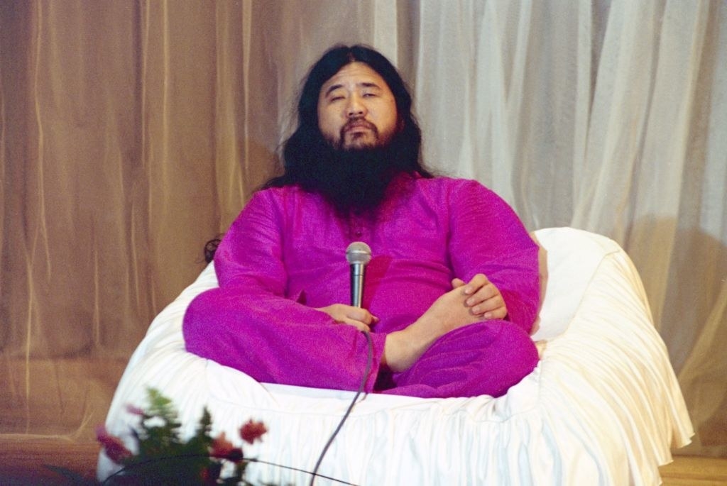 man with a beard and long hair sitting crossed legged in a bean bag-like chair holding a microphone