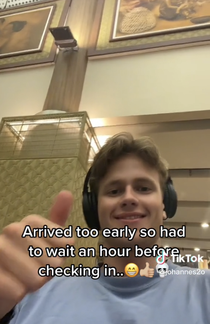 Man smiling and giving a thumbs-up with caption &quot;Arrived too early so had to wait an hour before checking in&quot; with big smile, thumbs-up, and skull emojis