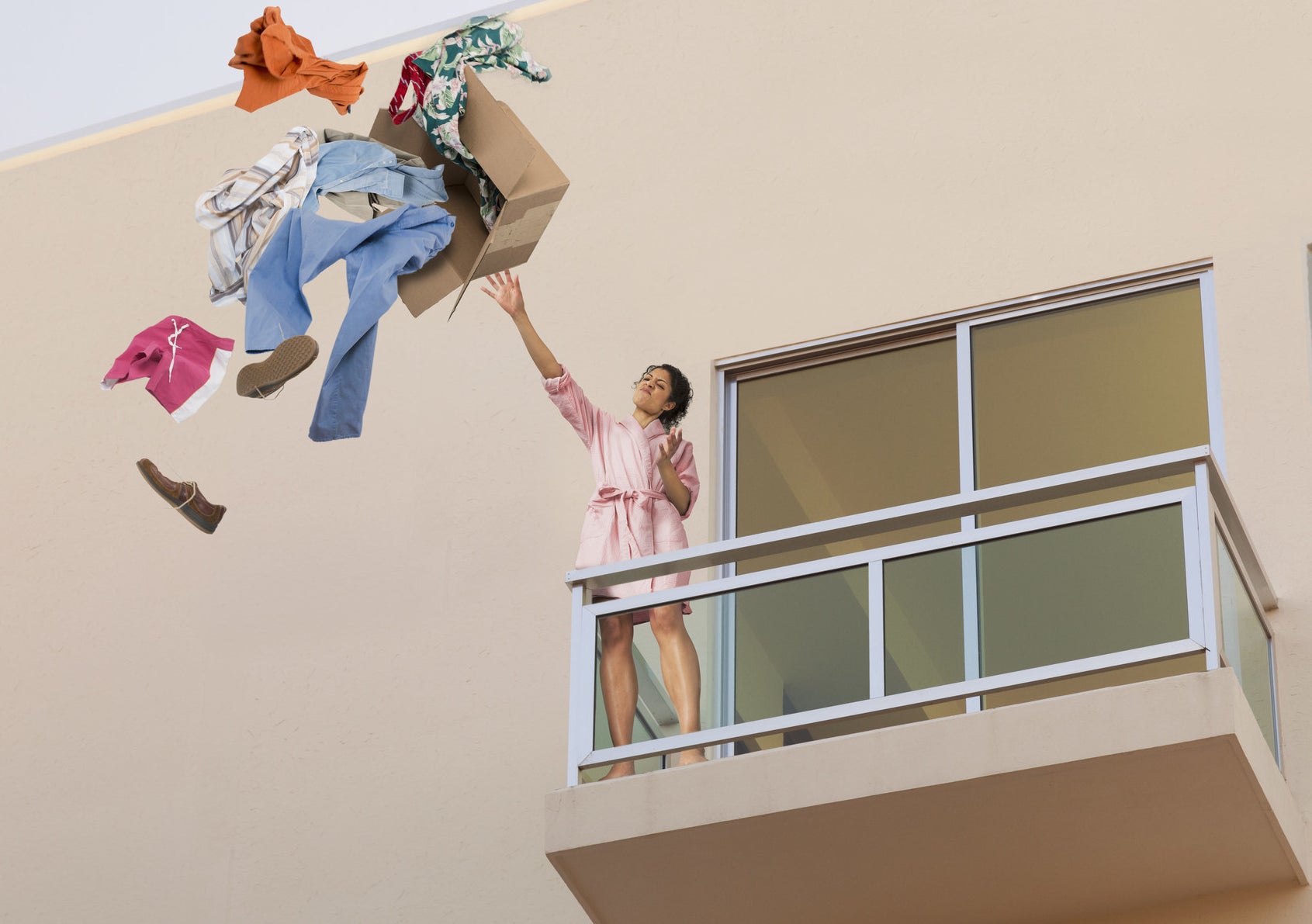 A woman throwing a box of clothes off her balcony