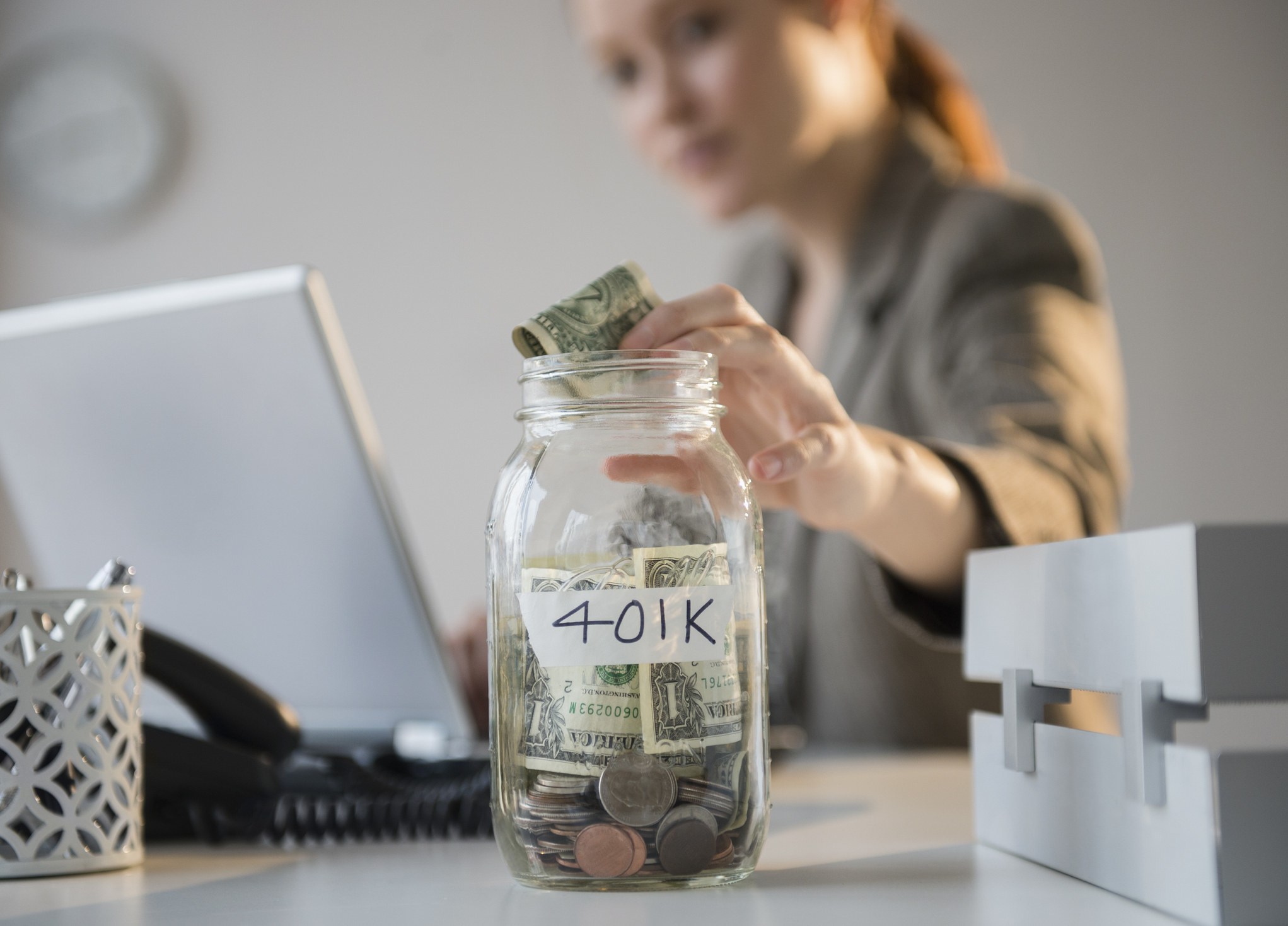 A woman putting a dollar into a jar that says &quot;401k&quot;