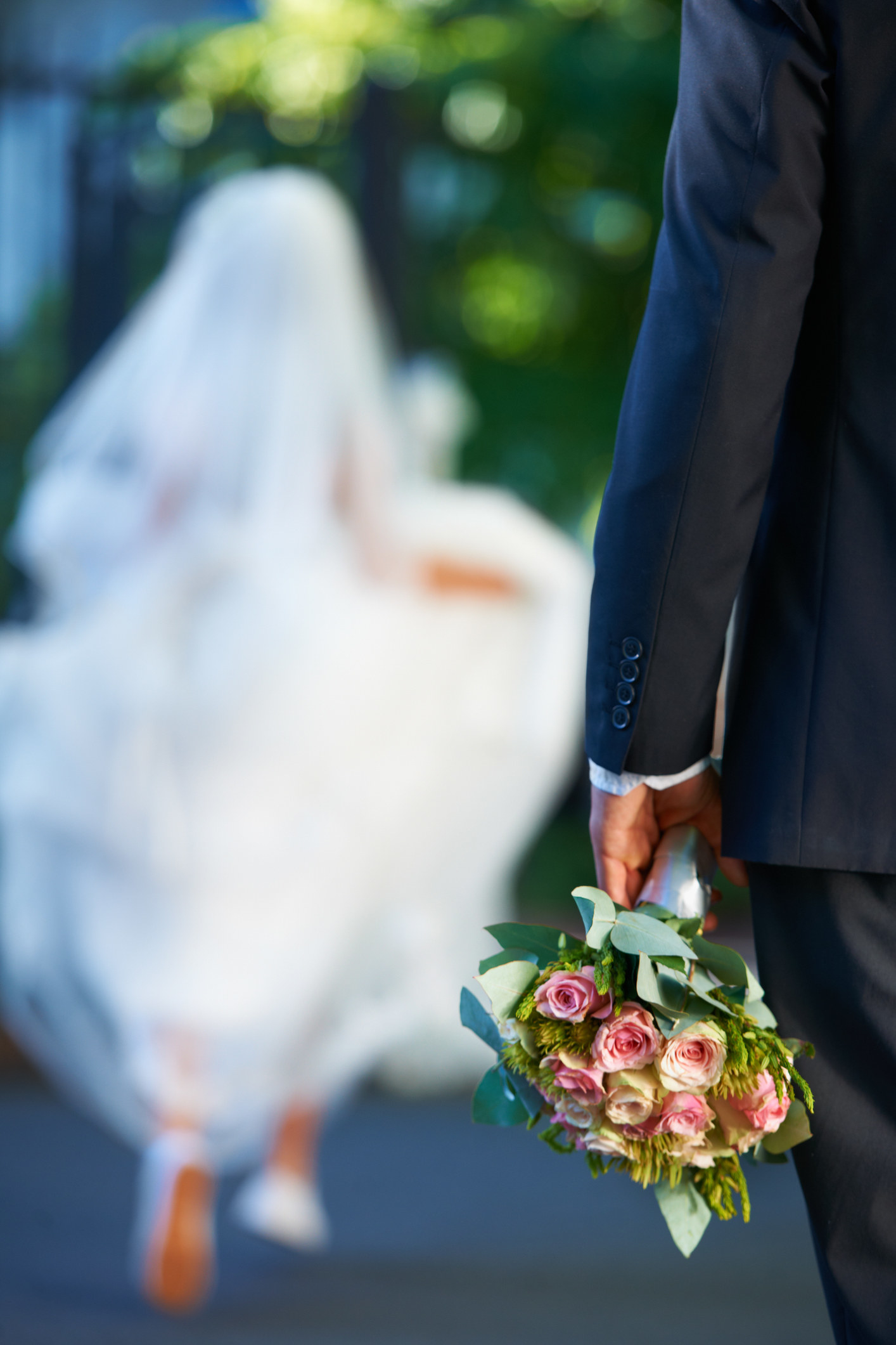 A groom holding a bouquet with their bride in the background