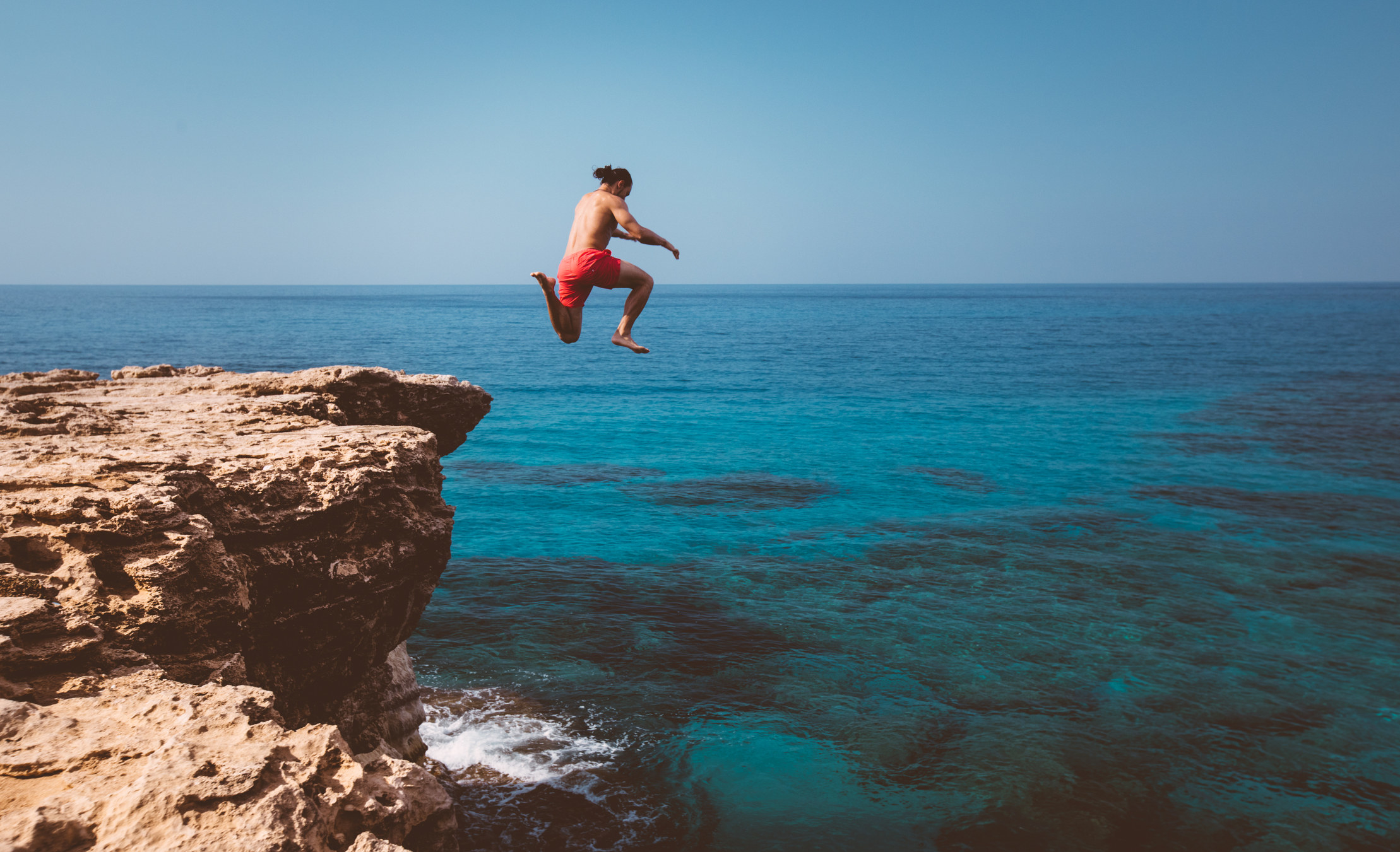 A man jumping off a cliff into the ocean