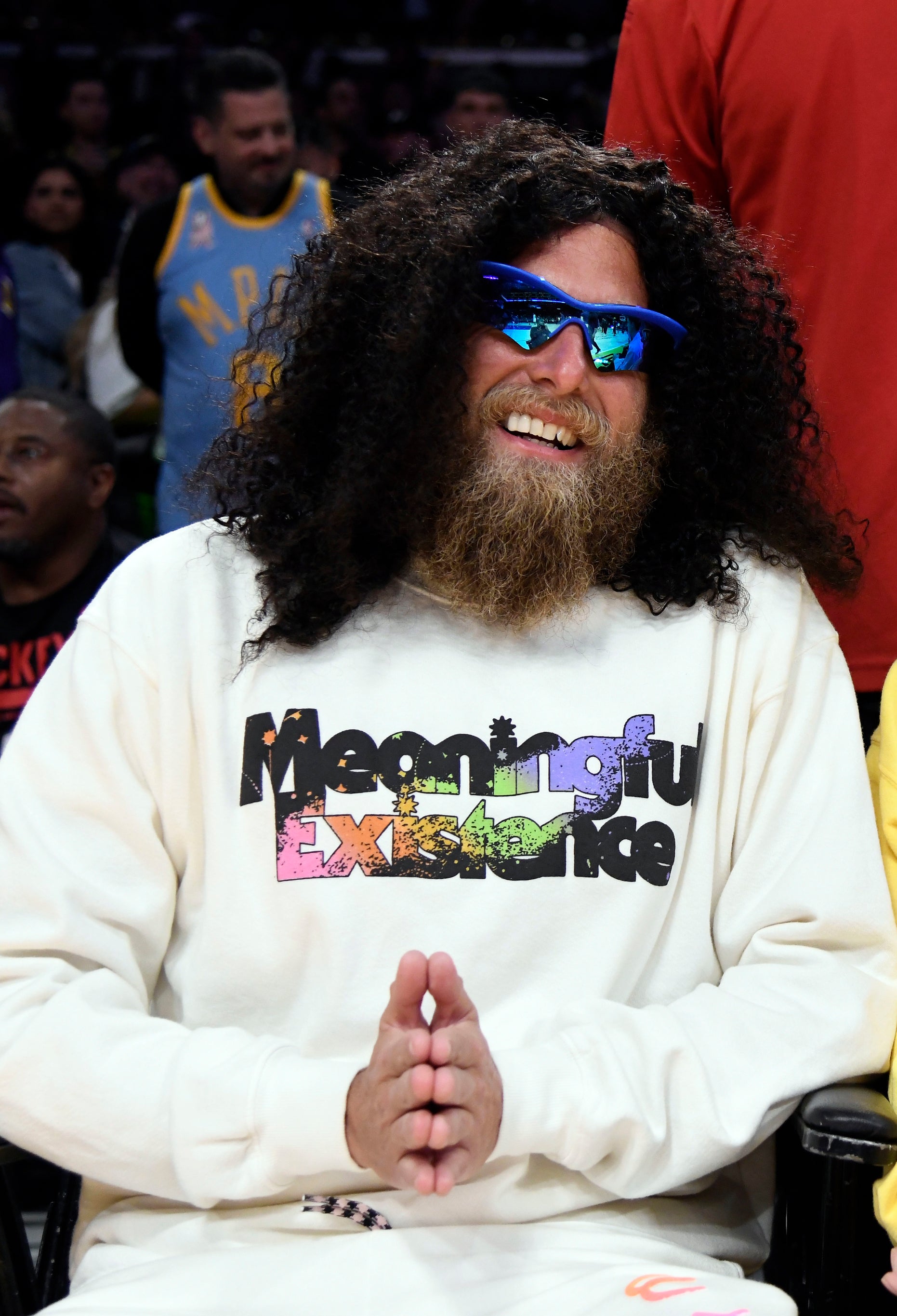 Close-up of Jonah wearing a long wig and sunglasses and a &quot;Meaningful Existence&quot; T-shirt