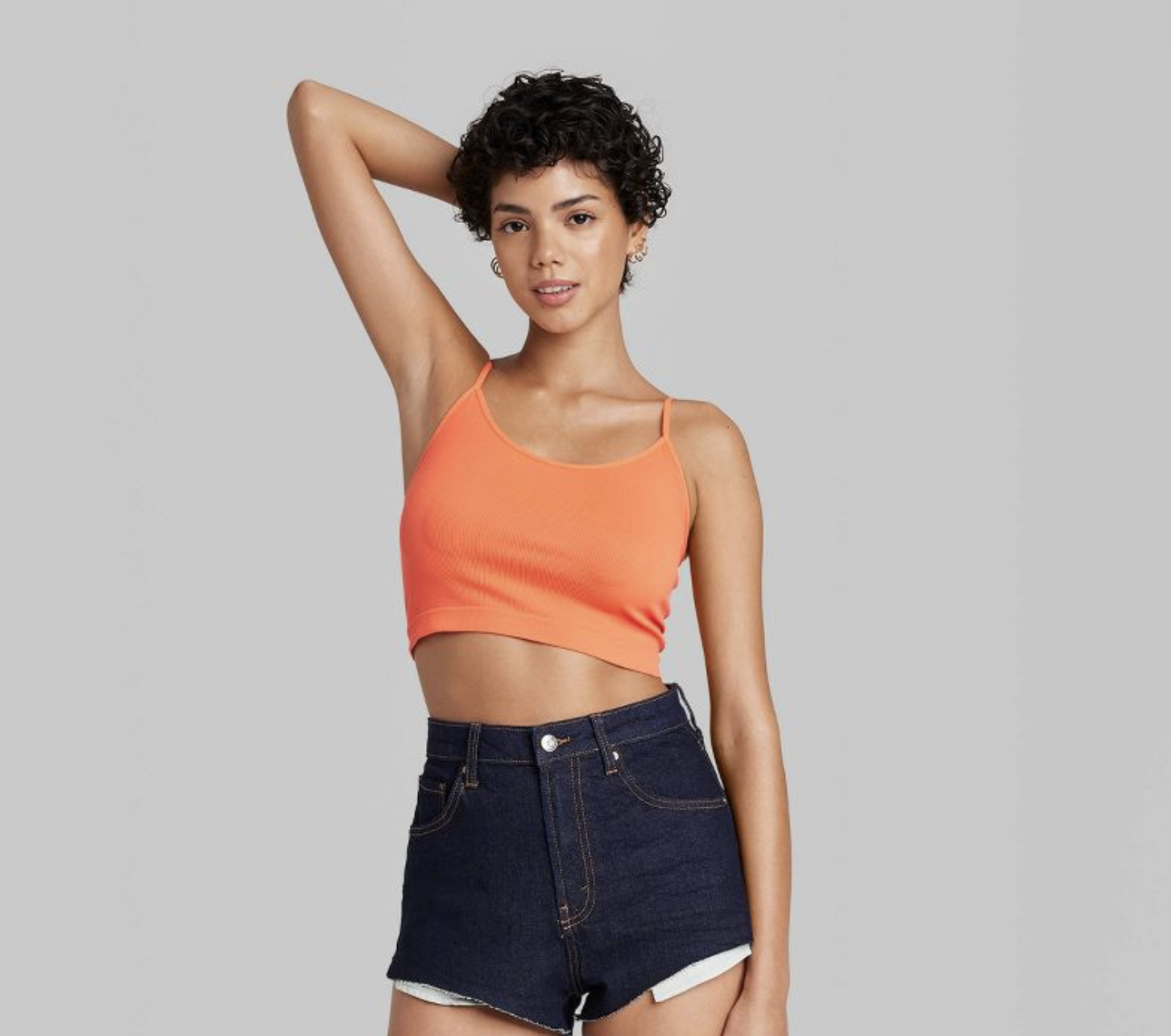 A person with curly brown hair wearing the bralette in orange