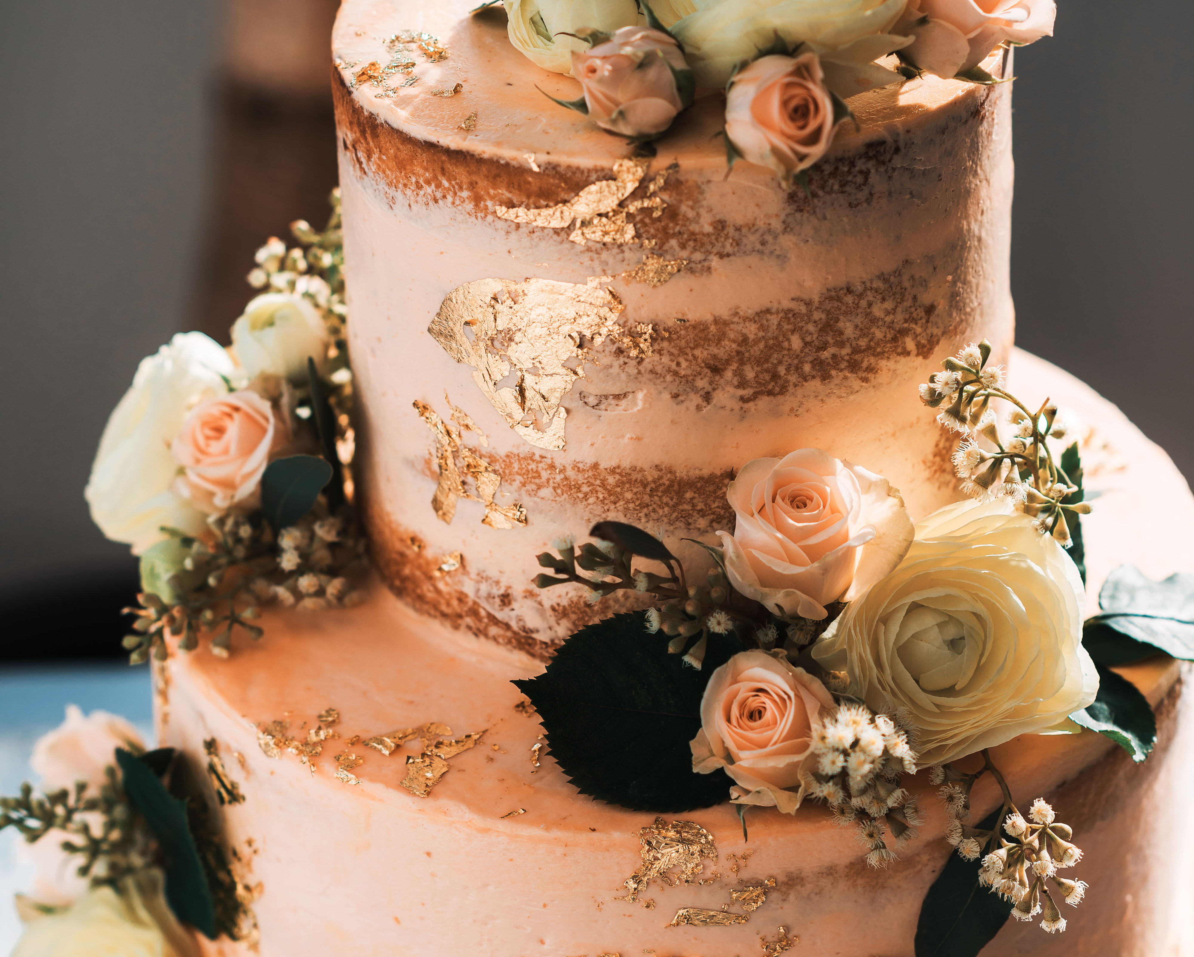 Close-up short of a naked wedding cake with floral and gold accents
